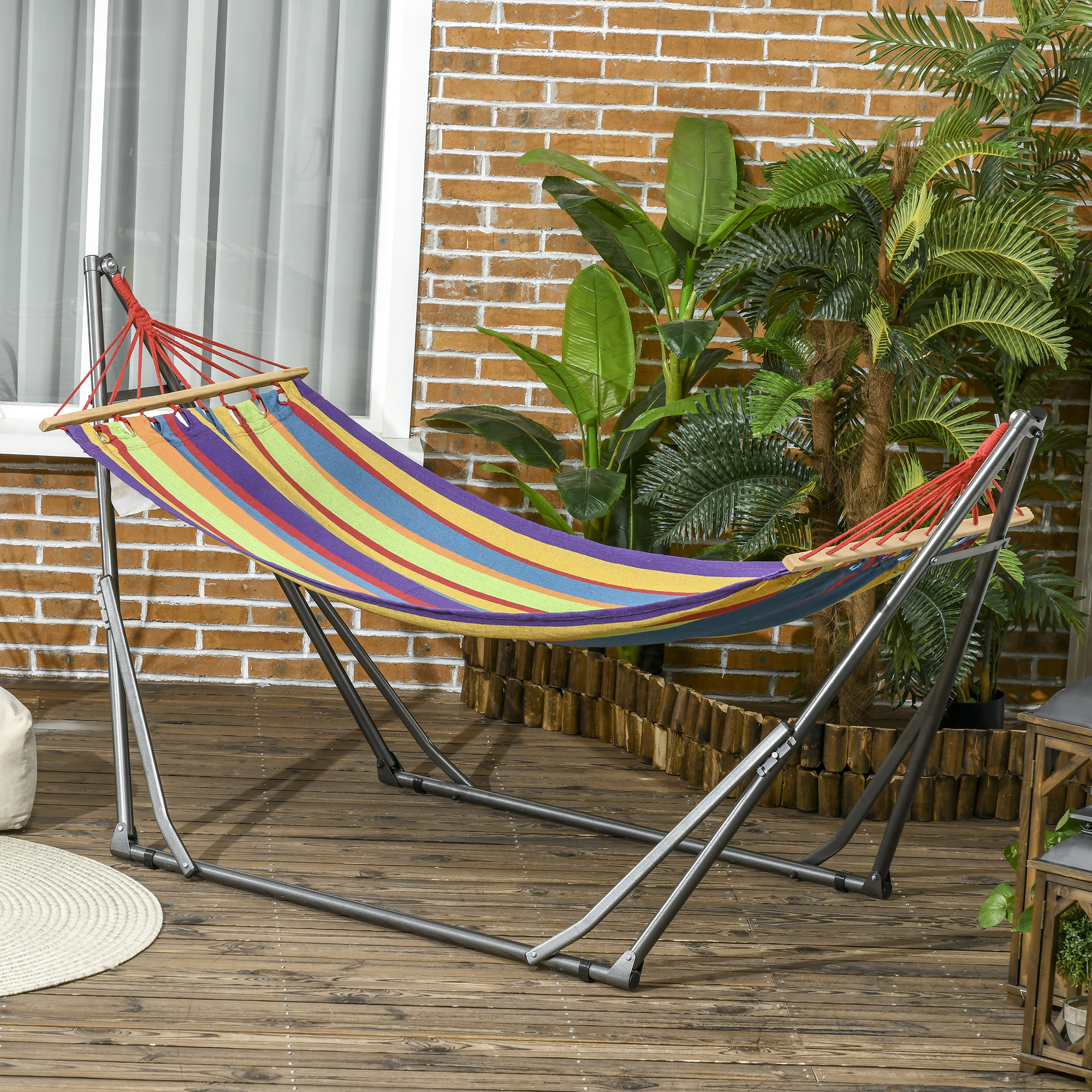 Una hamaca colorida a rayas cuelga de un soporte metálico en una terraza de madera.