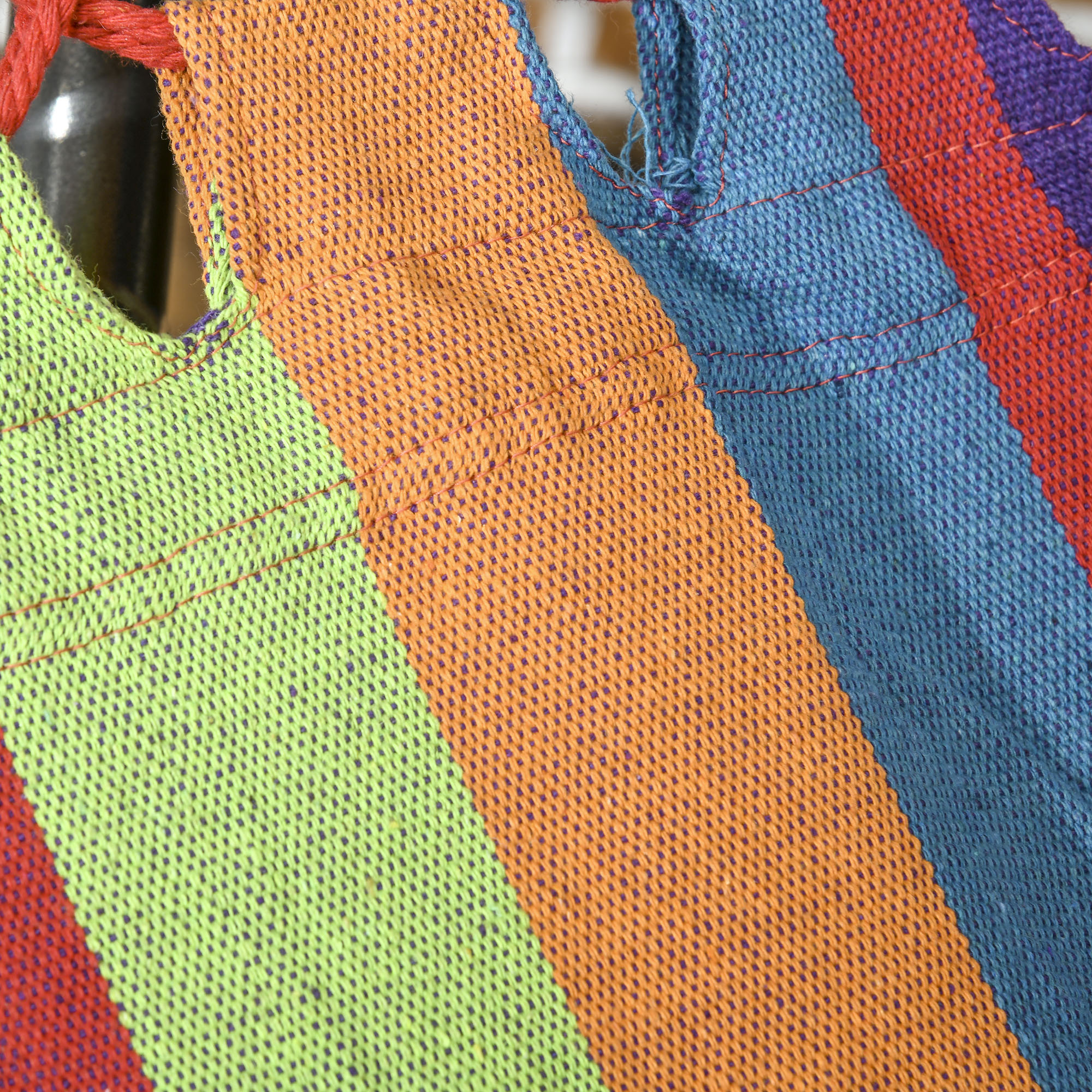Hamaca de tela colorida a rayas con costuras rojas.