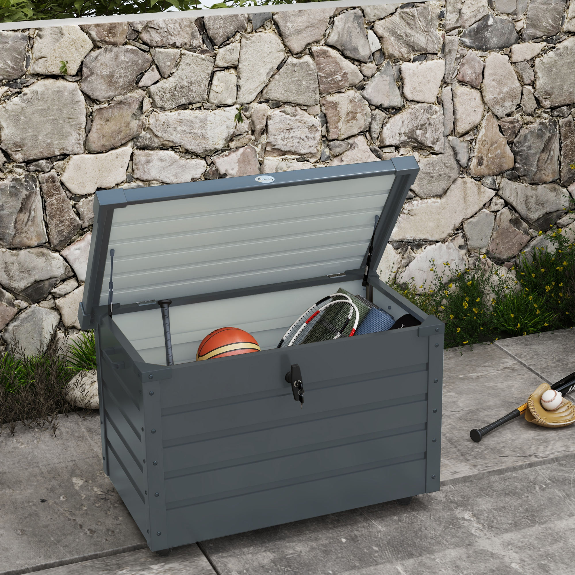 Caja de almacenamiento gris con tapa abierta, contiene pelota, raquetas y esterilla.