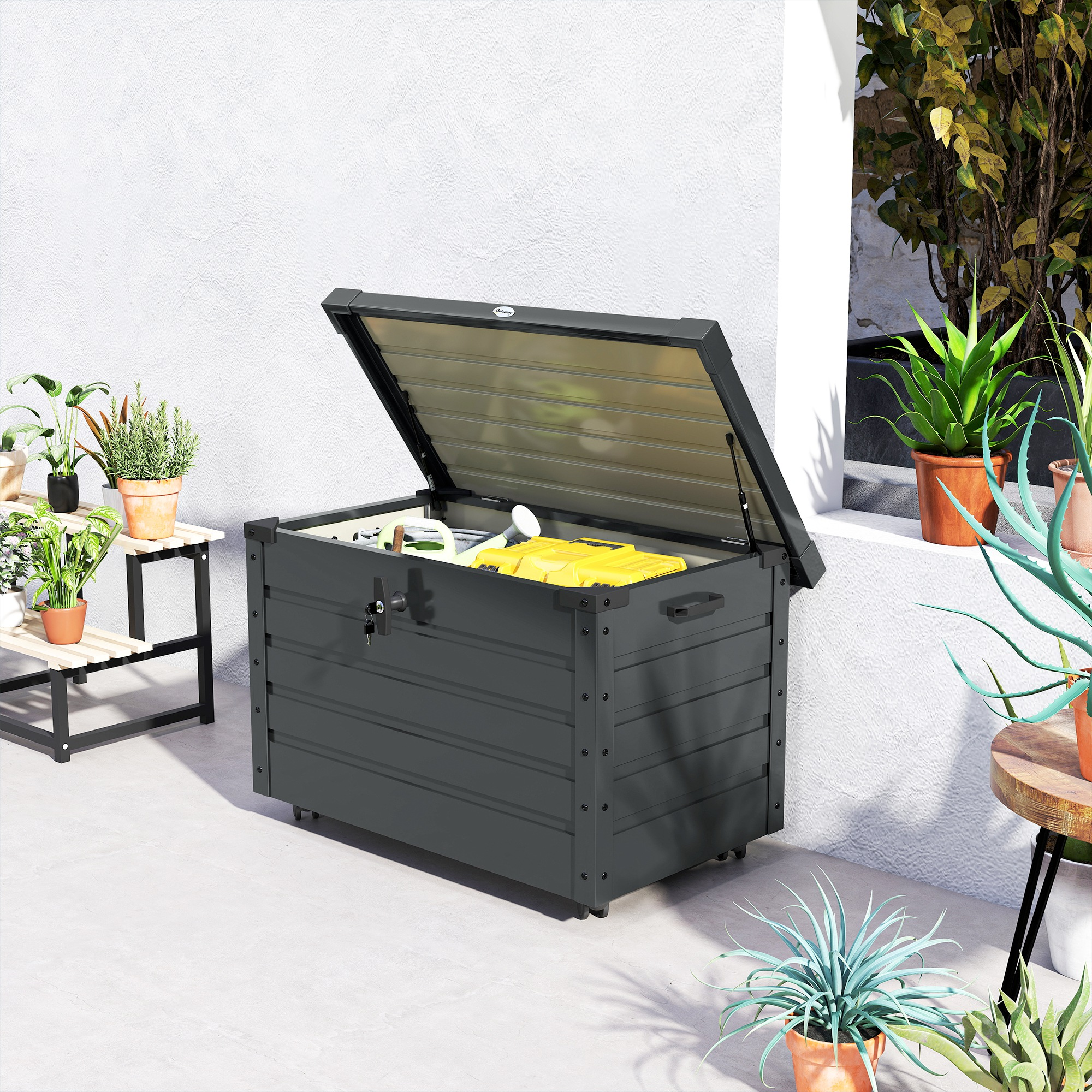 Caja de almacenamiento de jardín gris con tapa abierta, llena de objetos amarillos y verdes.