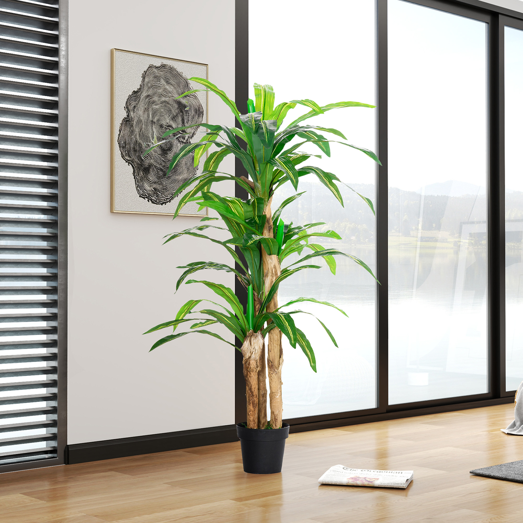 Planta alta en maceta con hojas verdes frente a ventana con vista a montañas.