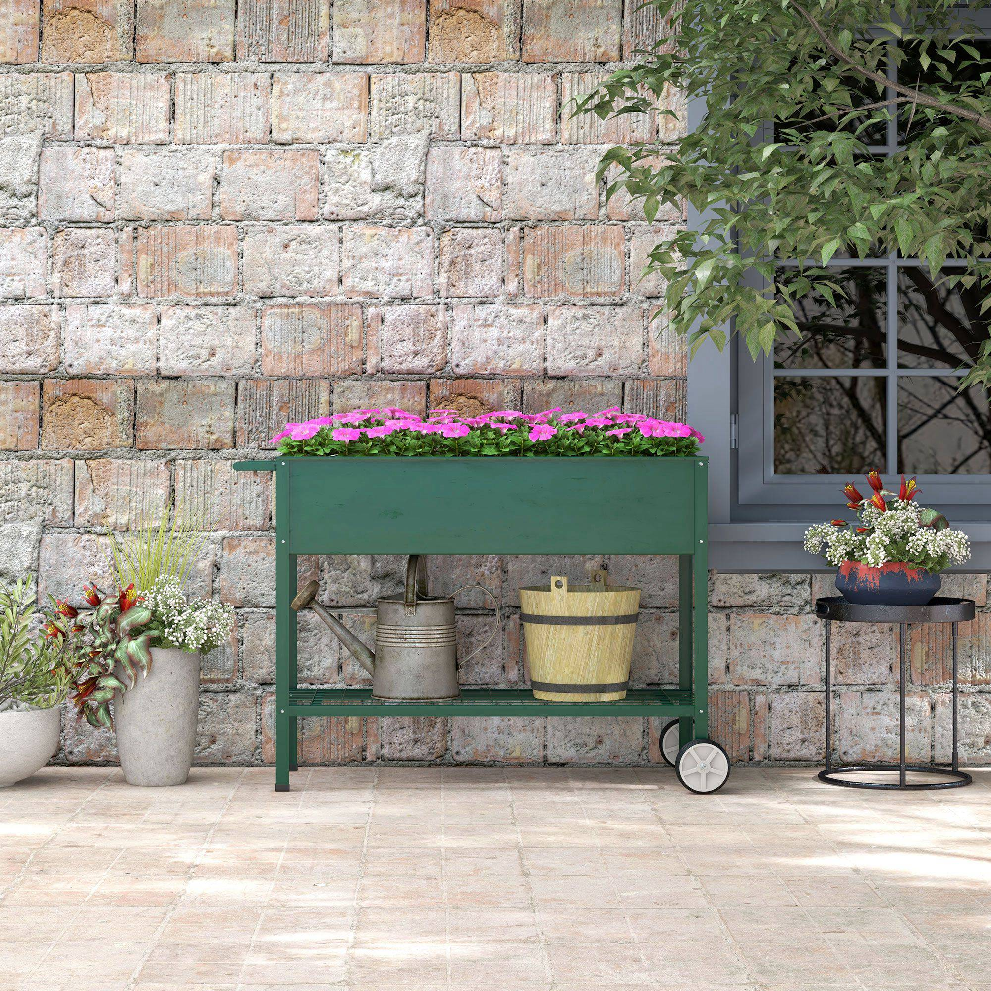 Una jardinera elevada verde con flores rosas junto a una ventana.