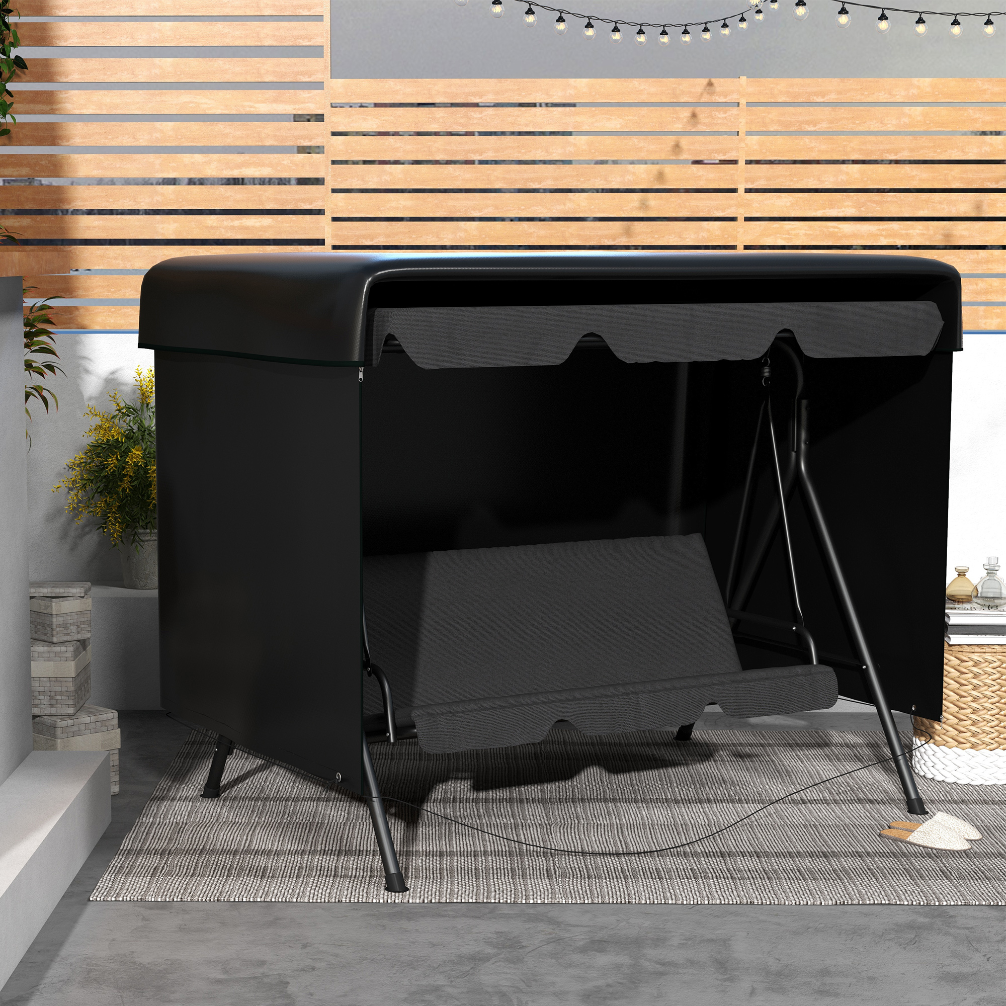 Una funda negra para columpio en un patio, con pared de madera y guirnalda de luces al fondo.