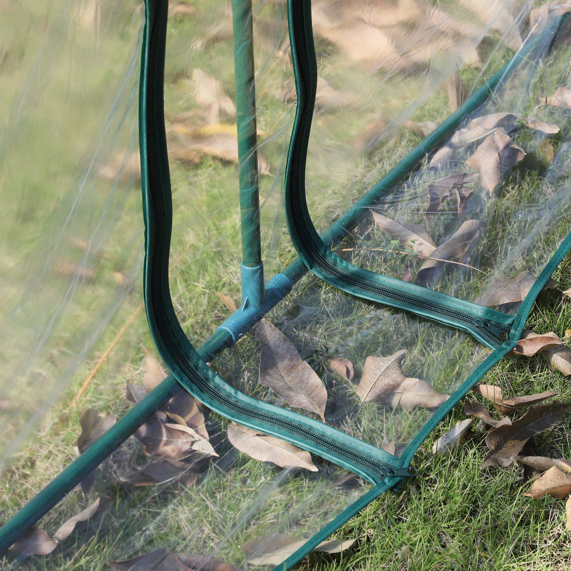 Estructura verde con cremalleras, cubierta de plástico transparente, sobre césped con hojas.