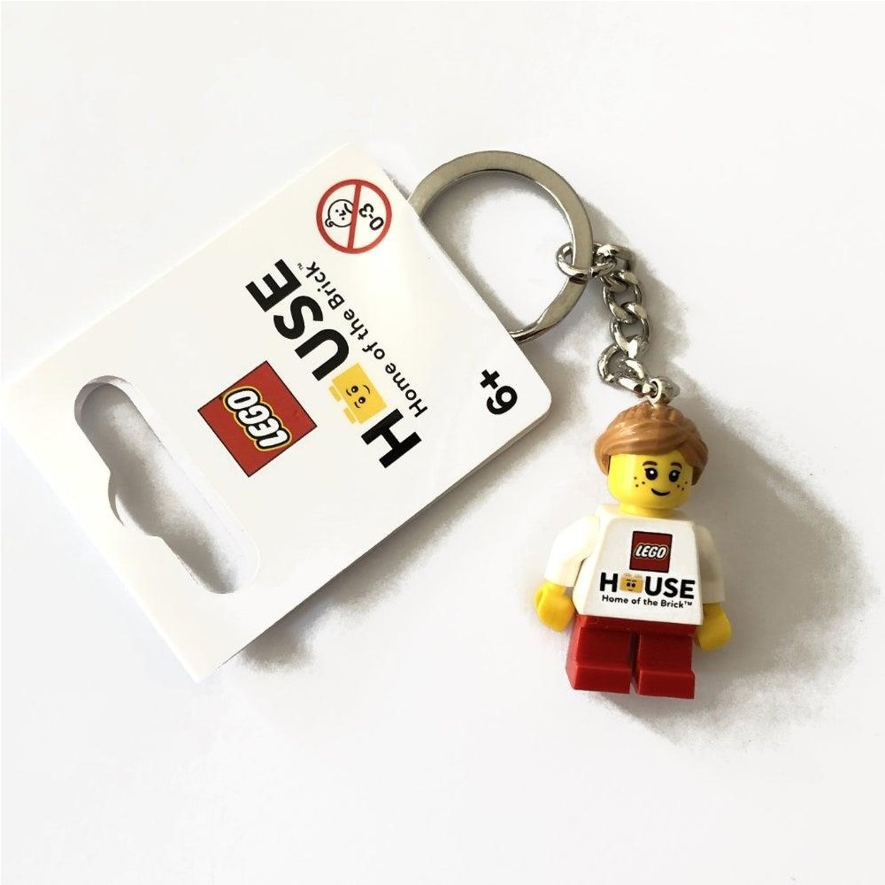 LEGO House anahtarlık, beyaz tişörtlü ve kırmızı pantolonlu bir minifigür.