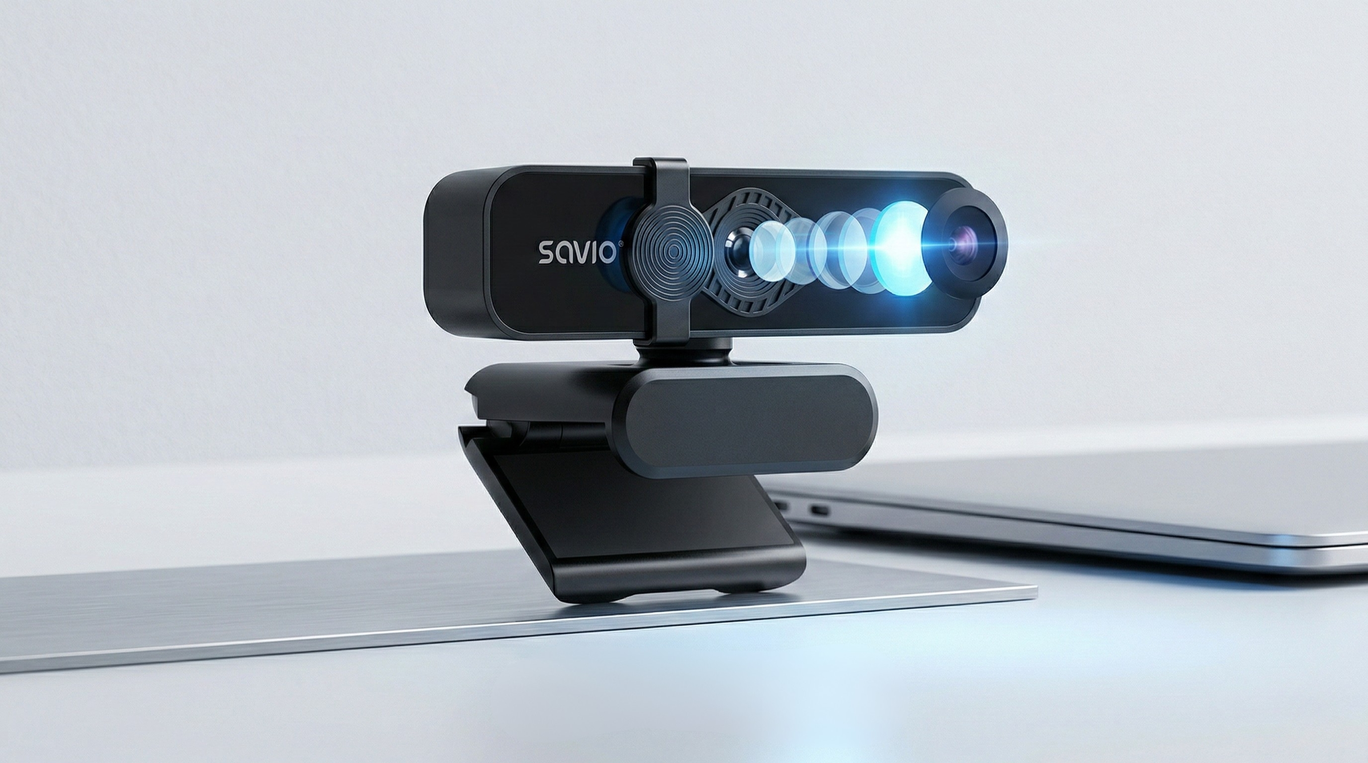 Czarna kamera internetowa z przezroczystymi soczewkami i laptopem na biurku.