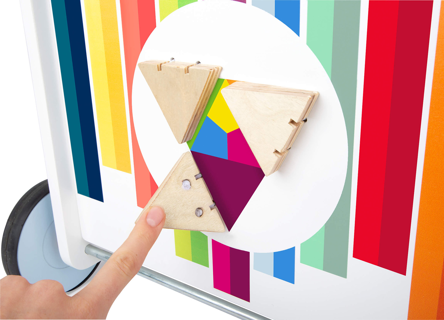 Ein Finger berührt ein dreieckiges Holzstück auf einem bunten Spielbrett.