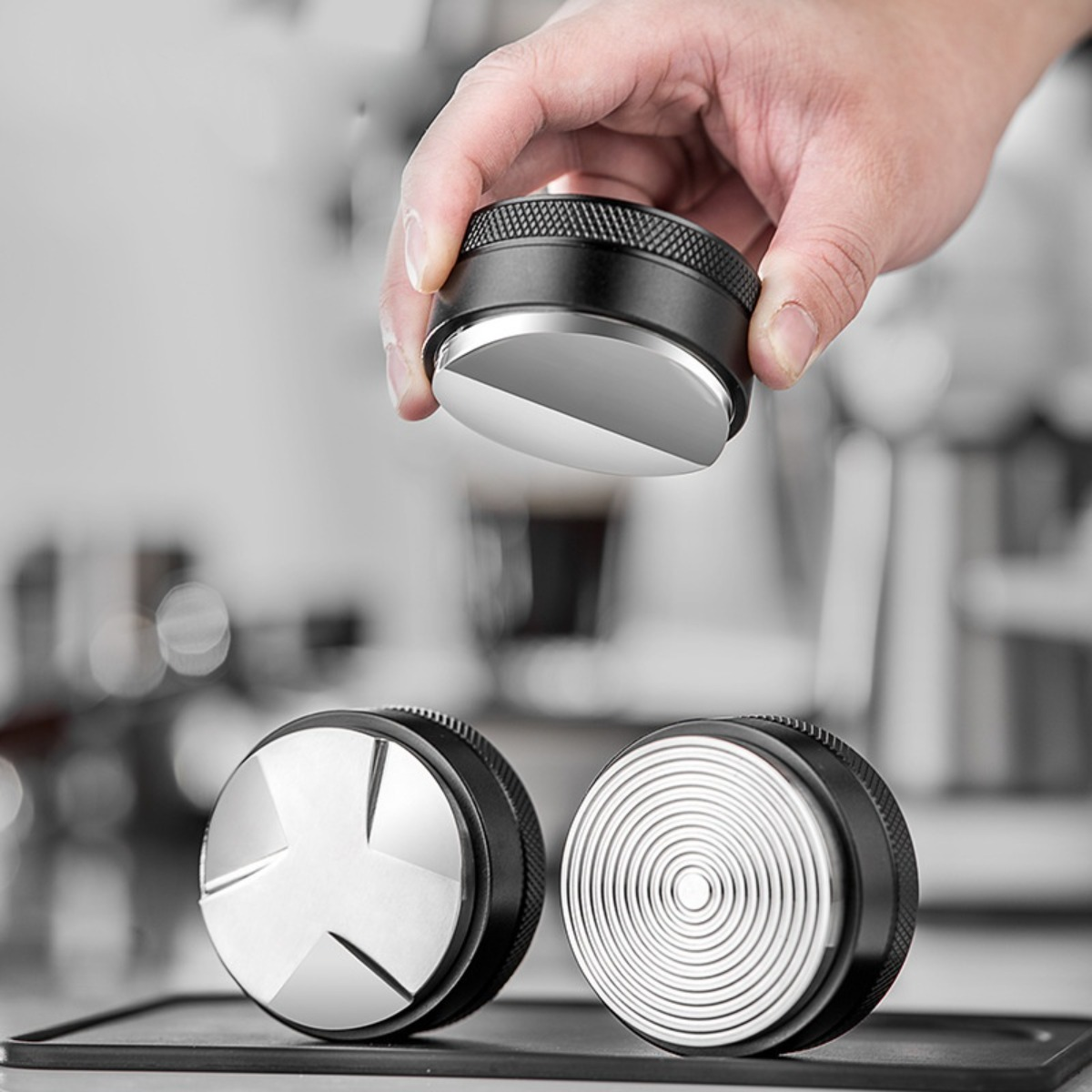 Una mano tiene un pressino da caffè su altri due pressini su un tappetino.