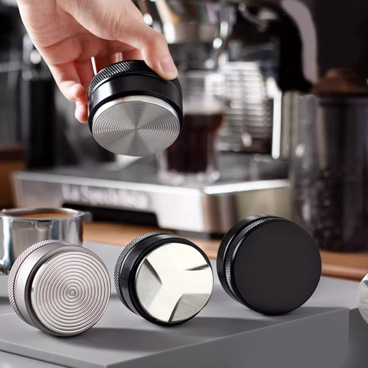 Mano tiene pressino nero con base argento sopra macchina da caffè.