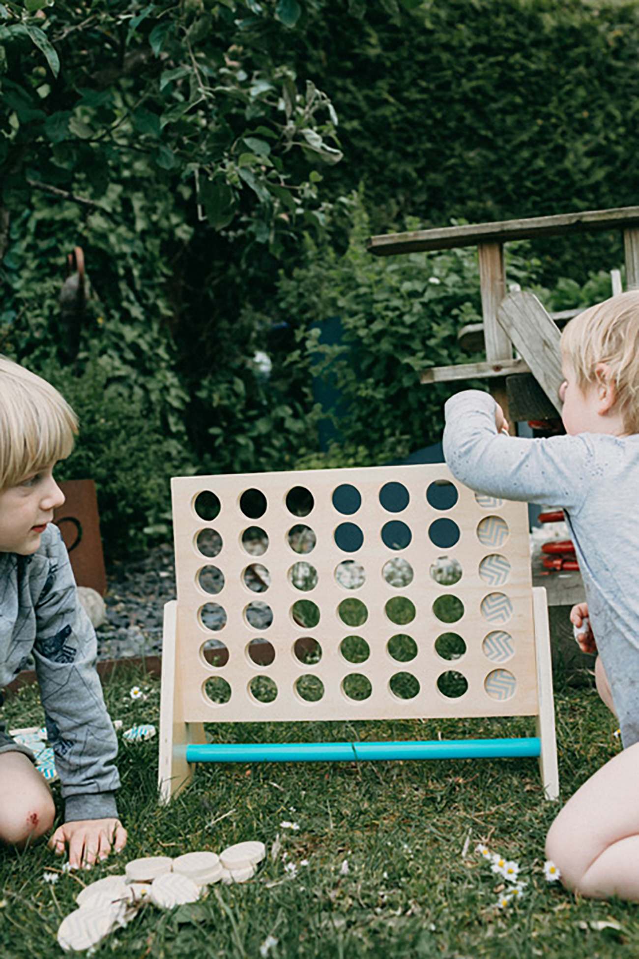 Zwei Kinder spielen Vier gewinnt auf dem Rasen in einem Garten. Ein Kind steckt ein Teil ein.