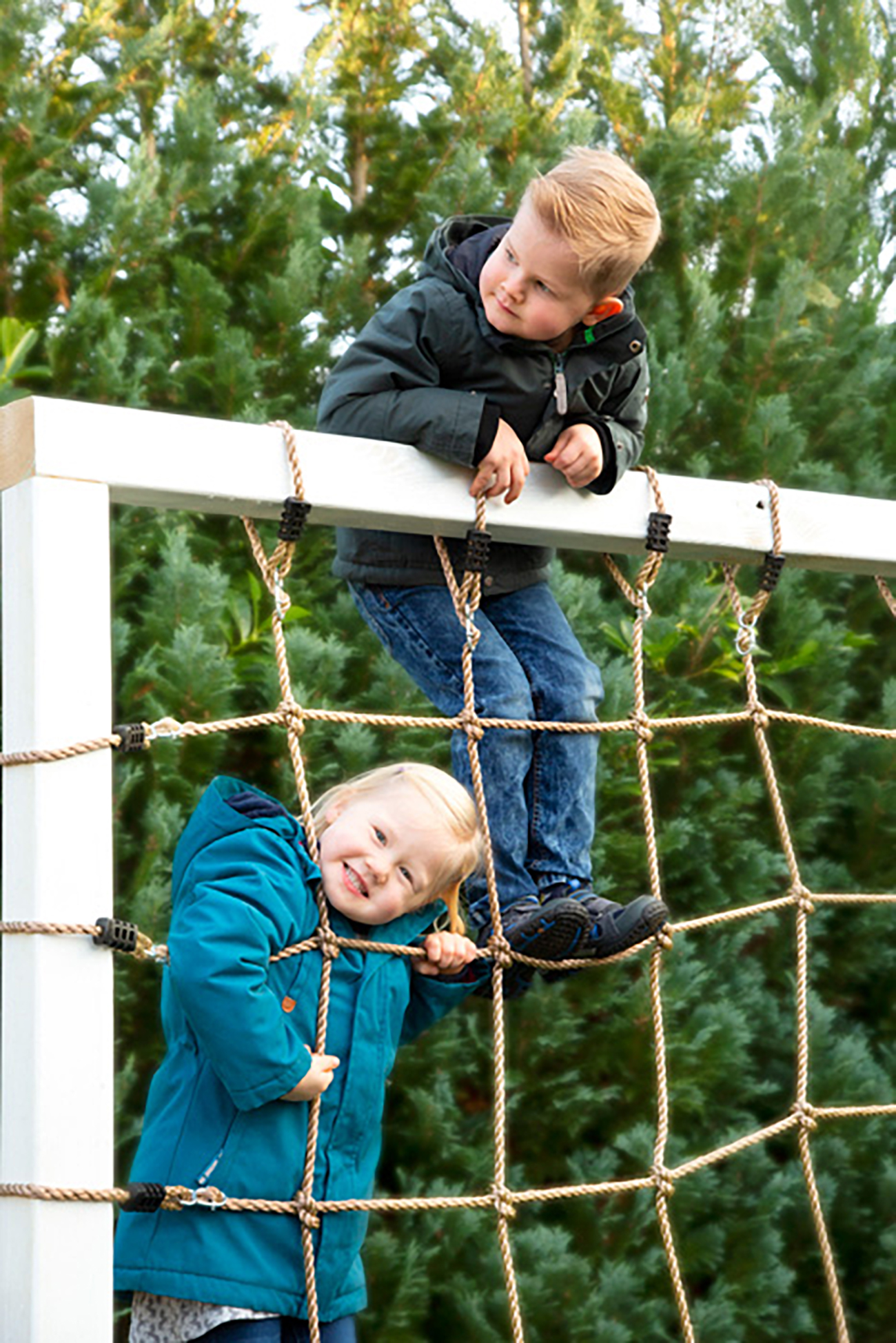 Zwei Kinder auf einem Klettergerüst vor Bäumen.
