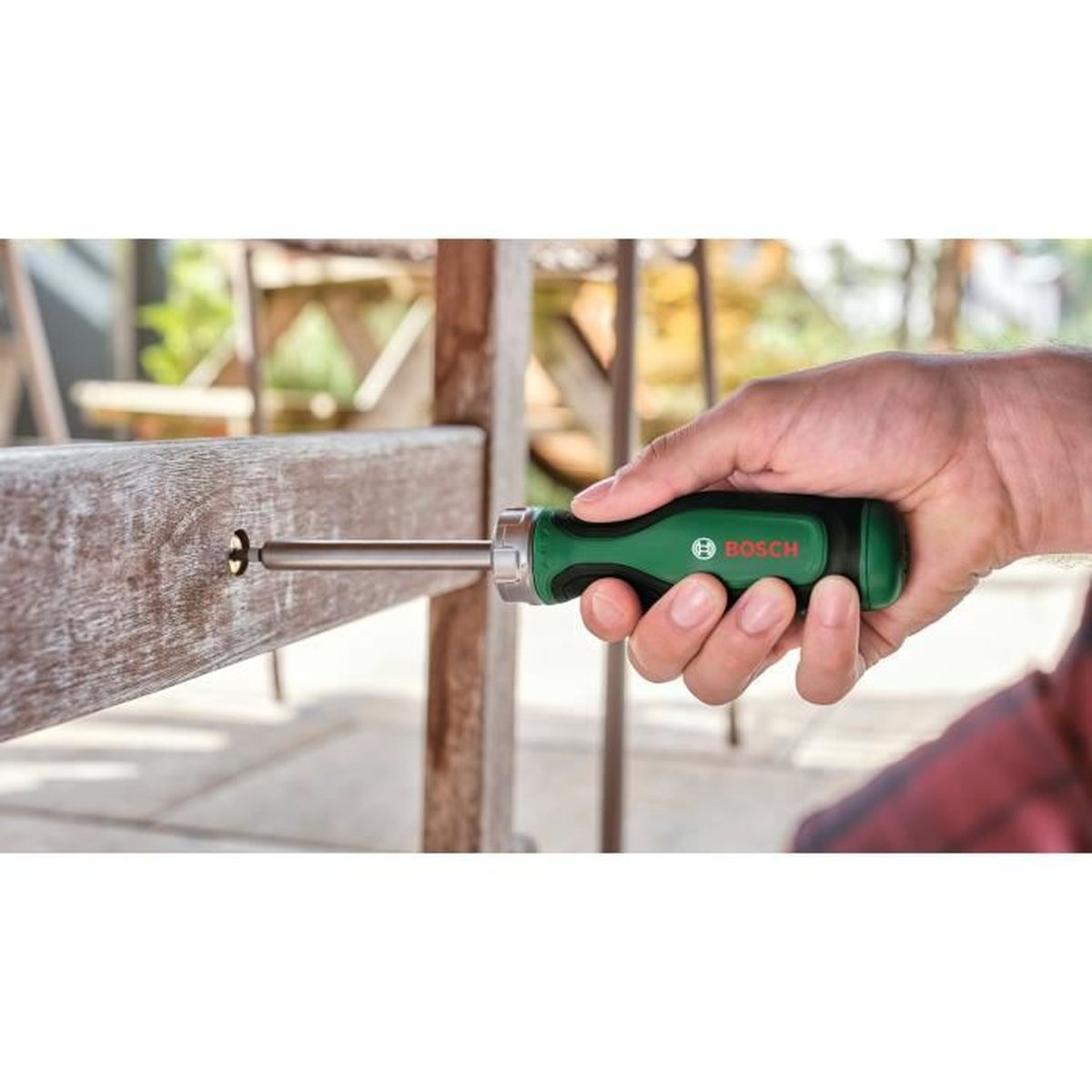 Una mano tiene un cacciavite Bosch verde, usandolo su una superficie di legno all'aperto.