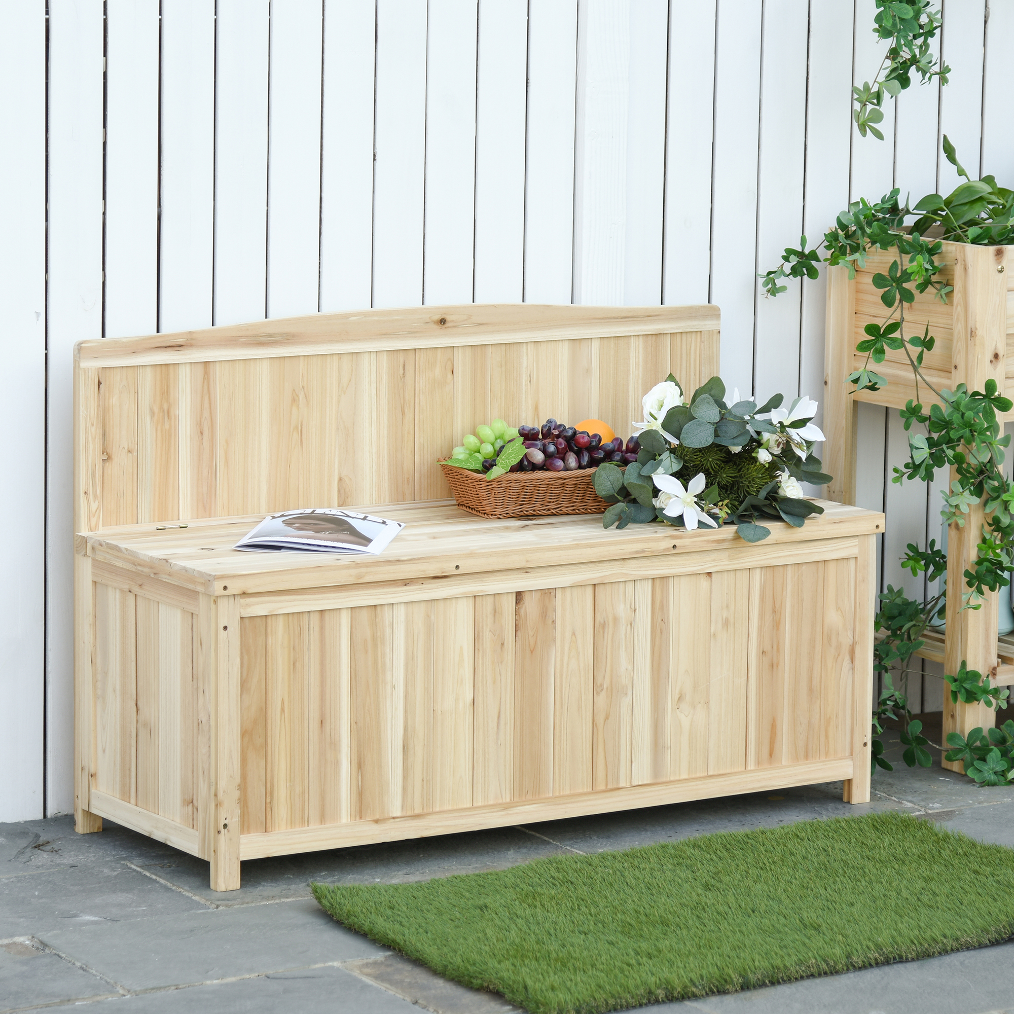 Banco de madera con cesta de fruta y ramo de flores frente a valla.