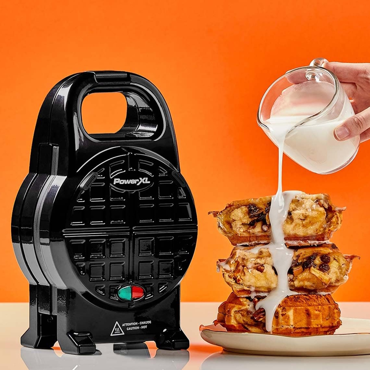 Ein schwarzer Waffelmaker mit gestapelten Waffeln, die mit Glasur übergossen werden.