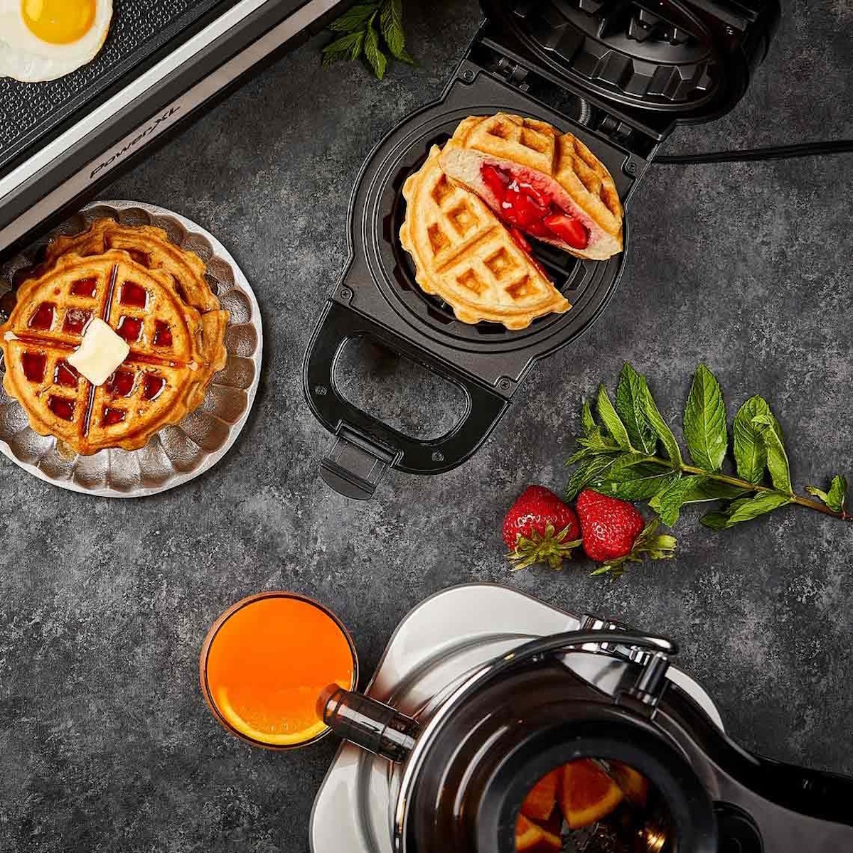 Ein Waffeleisen mit Waffeln, Erdbeeren, Saft und einem Ei.