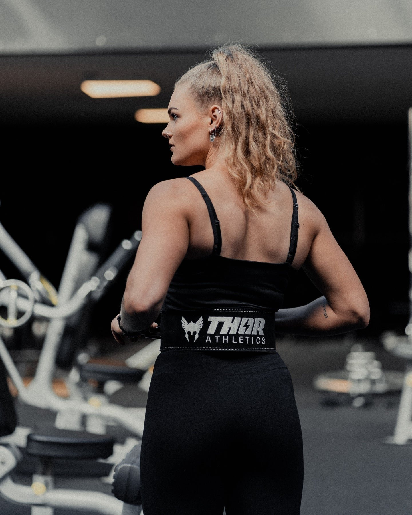 Femme à queue de cheval blonde porte une tenue de sport noire dans une salle de sport.