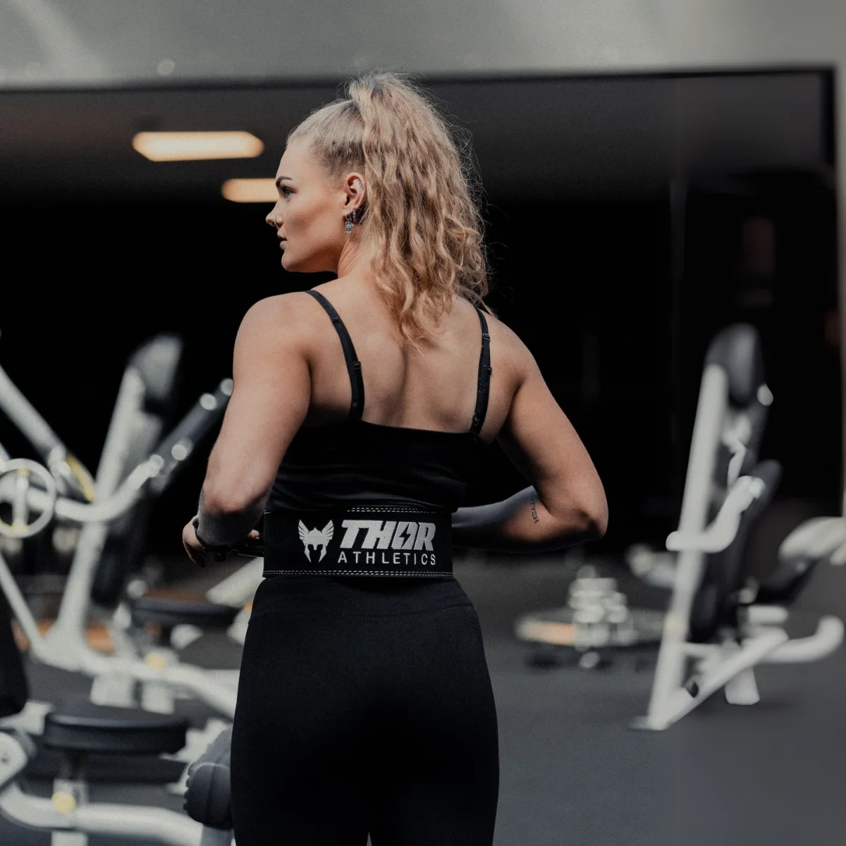 Femme en tenue de sport noire avec une ceinture de musculation dans une salle.