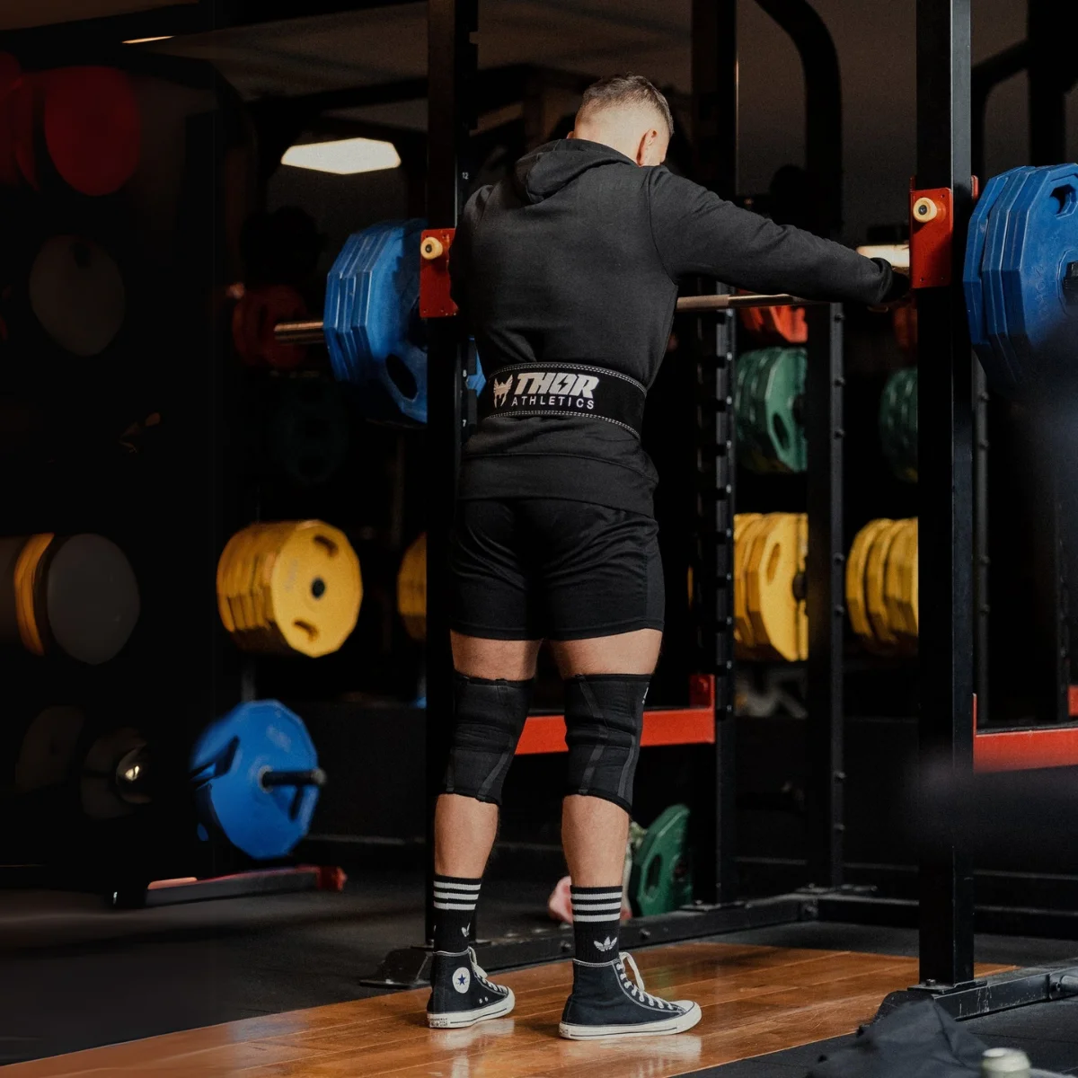 Un homme en tenue de sport se tient devant un rack de musculation avec des poids.