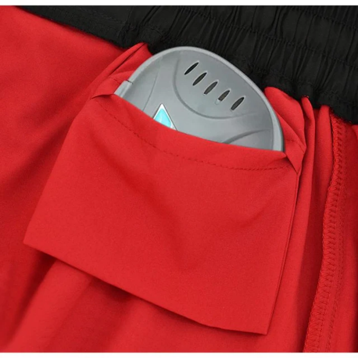 Un appareil gris avec des fentes est glissé dans la poche d'un short rouge.