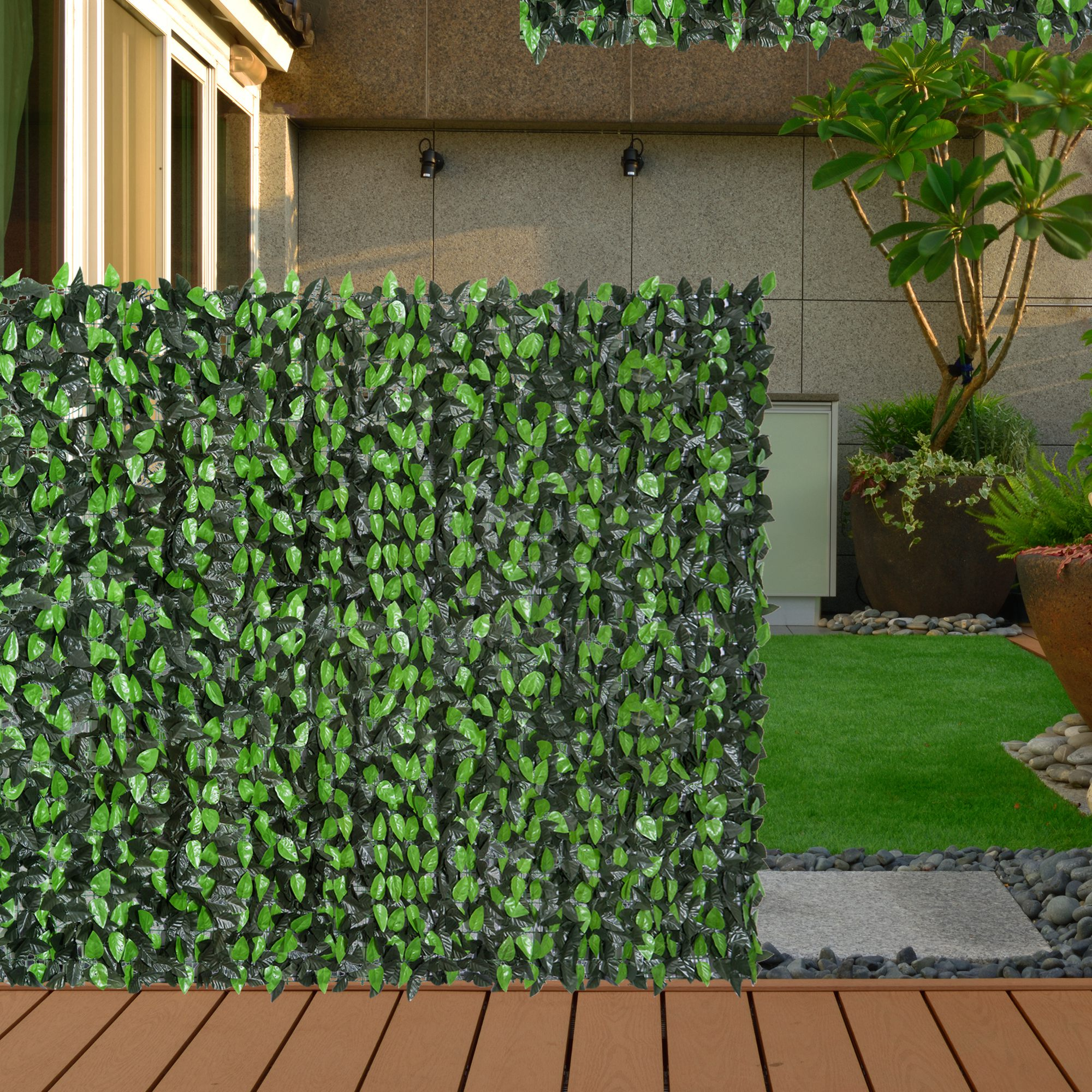 Una pantalla de privacidad de hojas verdes artificiales frente a una pared con terraza de madera.