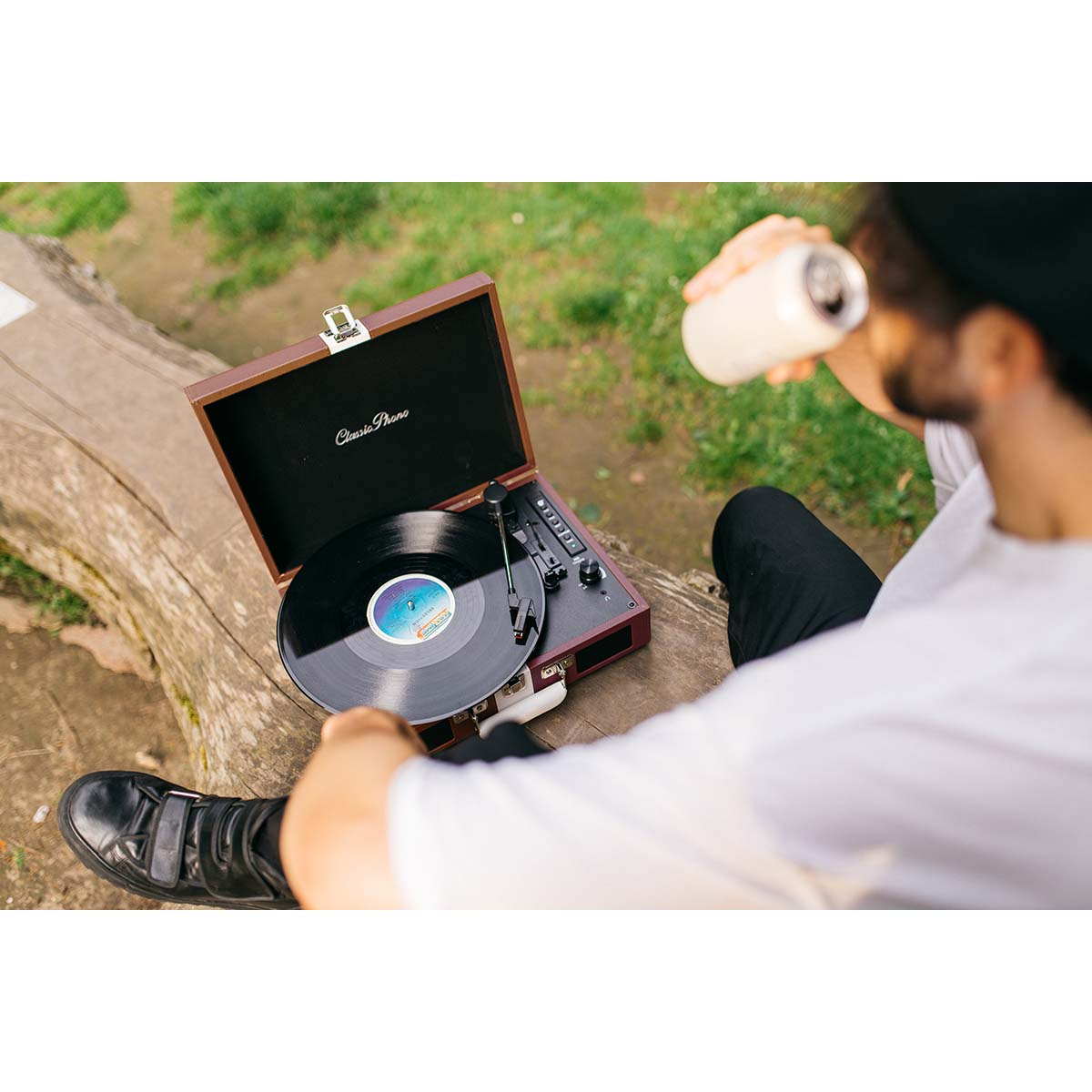 Mężczyzna pije z puszki obok gramofonu z płytą winylową na zewnątrz.