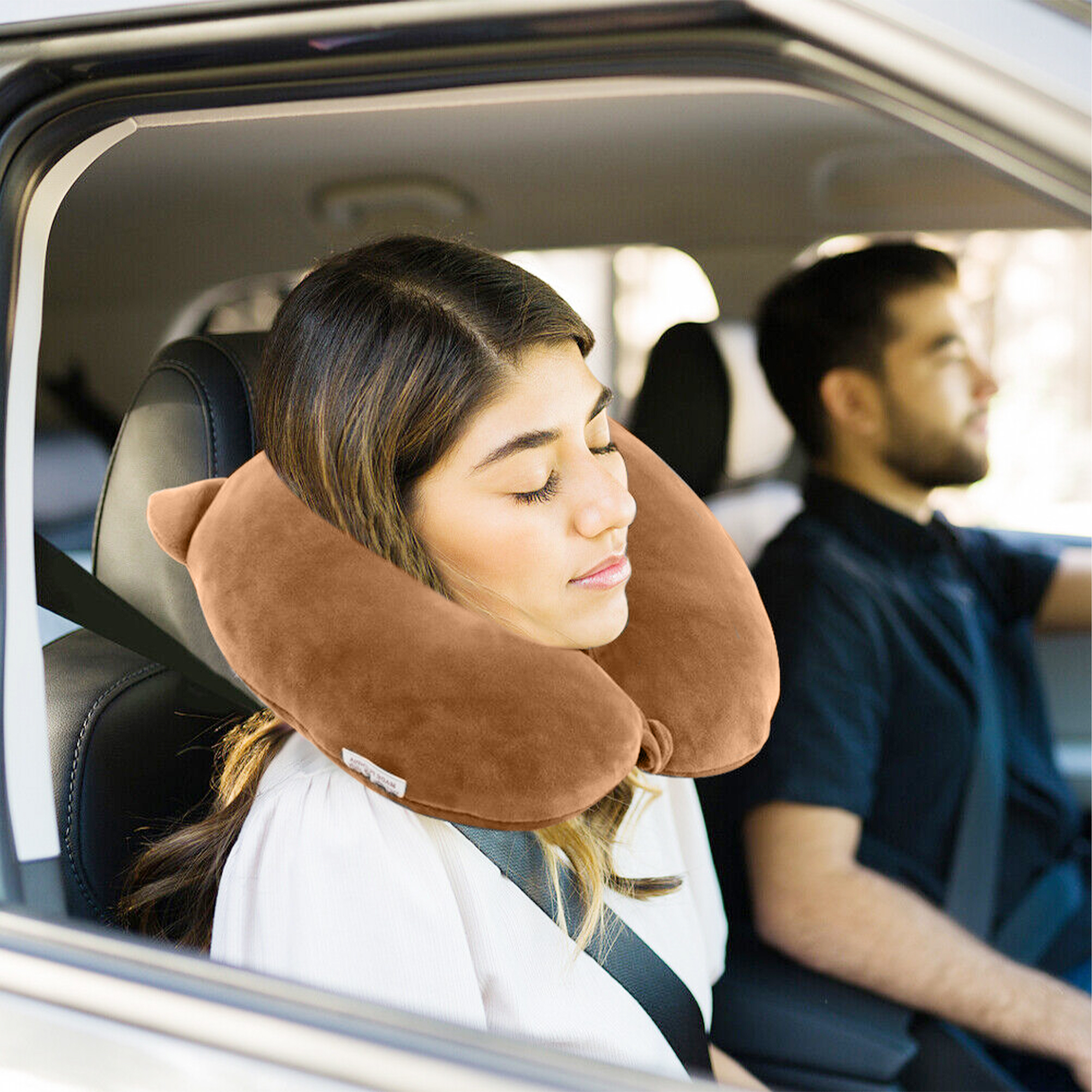 Una donna con cuscino da collo marrone dorme in auto, un uomo guida.