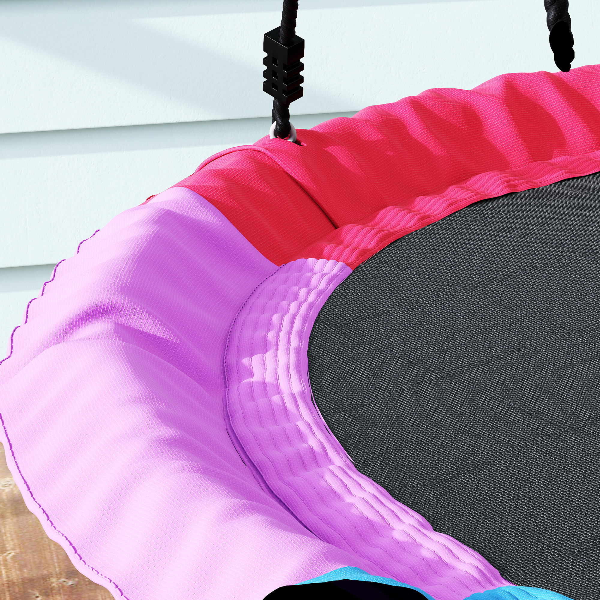 Un asiento columpio colorido con acolchado rosa y morado cuelga de una cuerda negra.