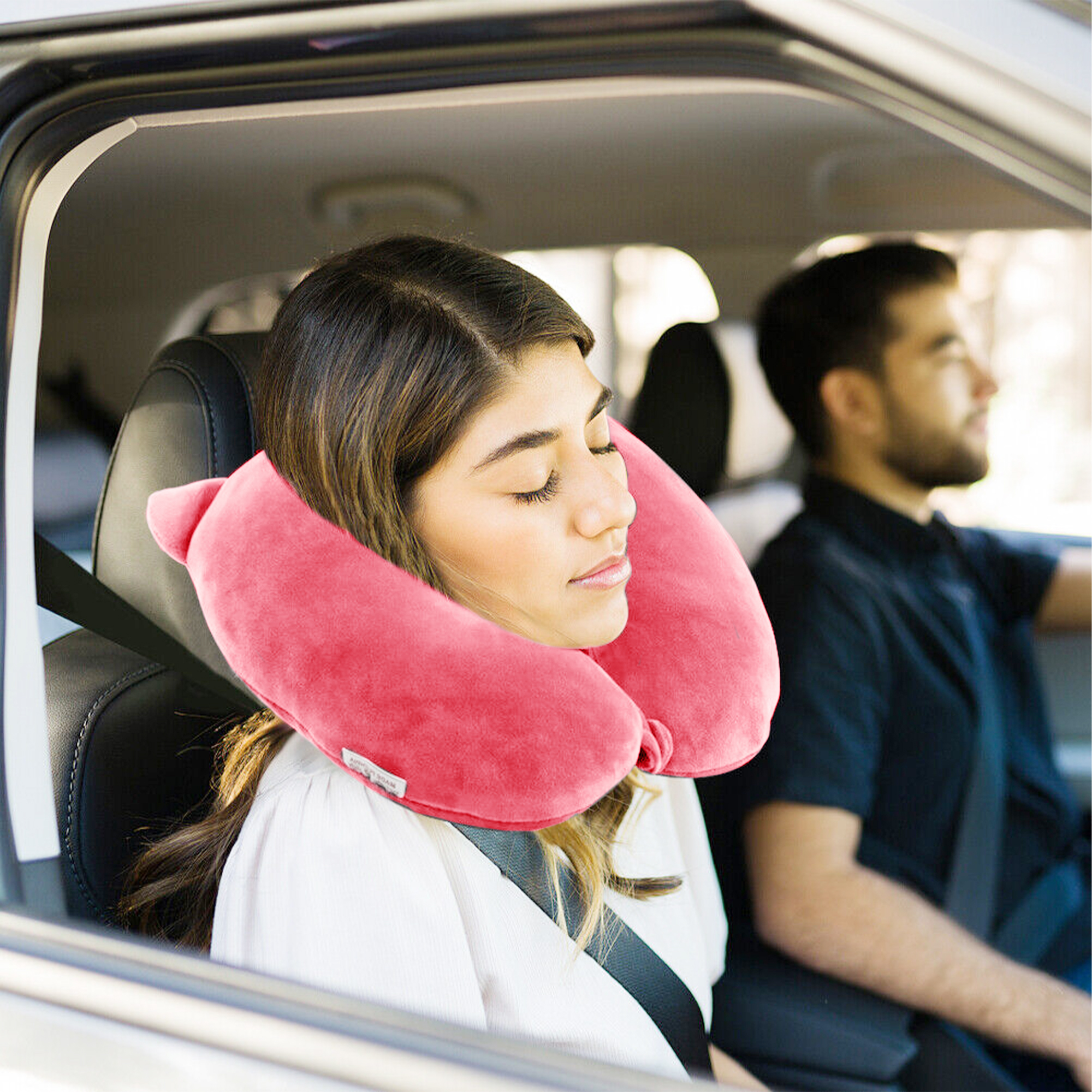 Donna con cuscino da viaggio rosa dorme in auto, uomo guida.