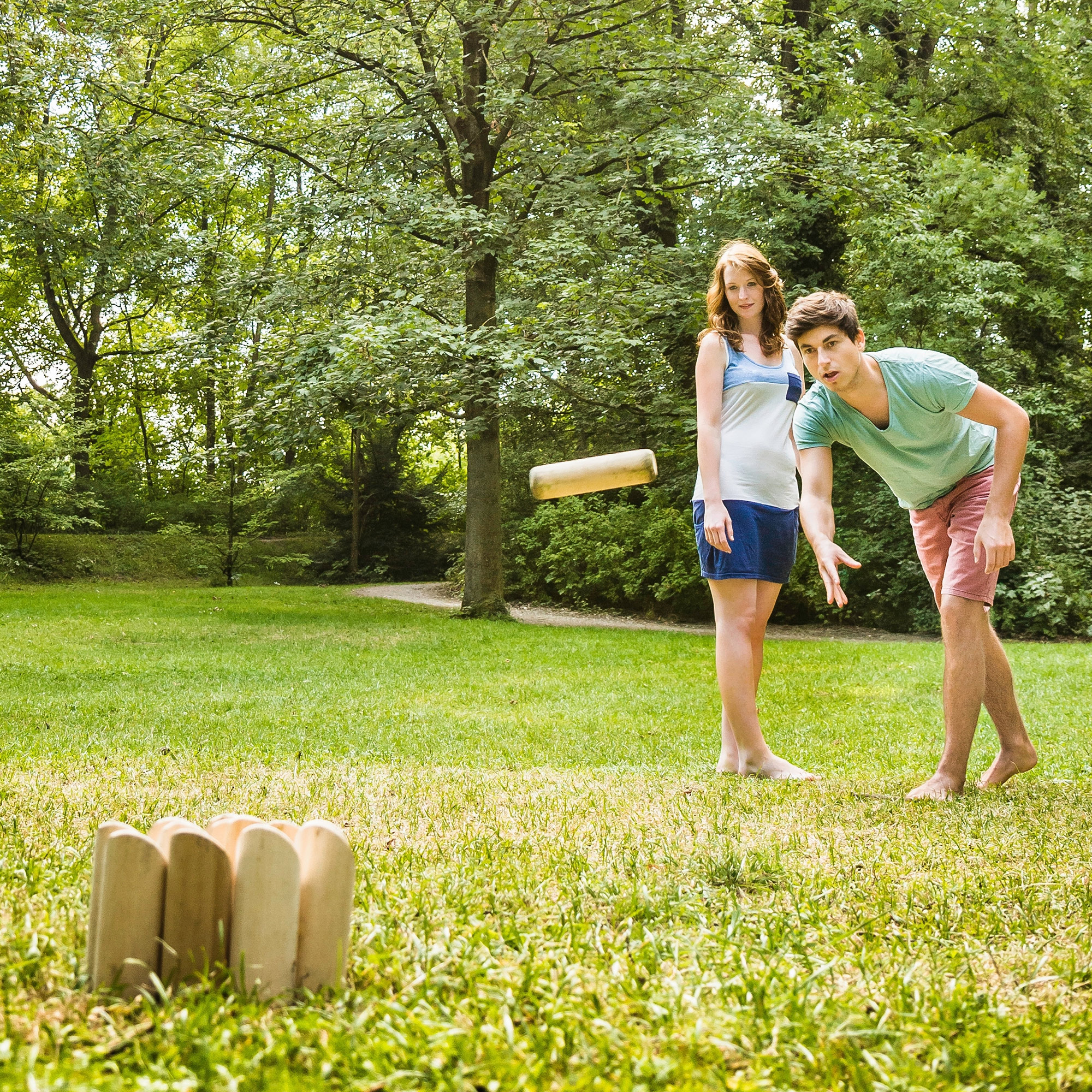 Un hombre y una mujer juegan al aire libre. Una pieza de madera vuela por el aire.