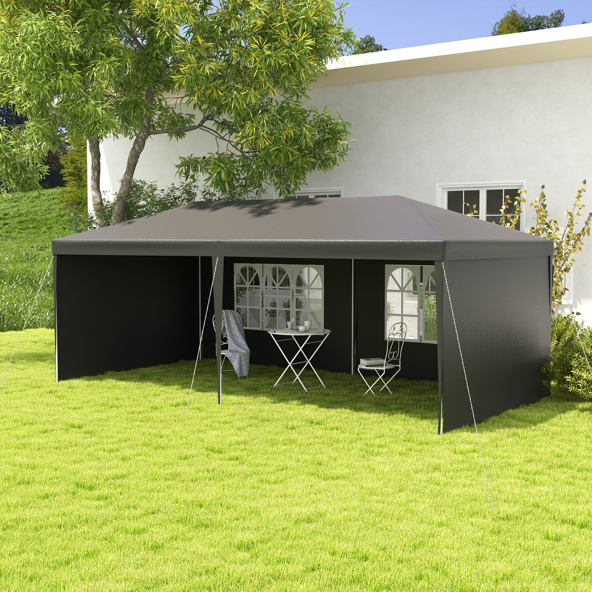 Una carpa negra con mesa y sillas está sobre un césped verde frente a una casa blanca.