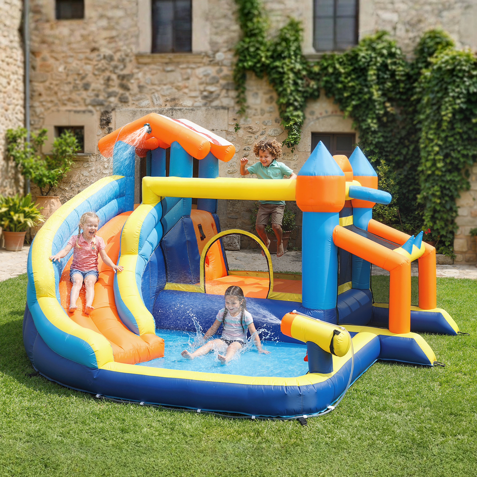 Niños juegan en un tobogán acuático colorido con piscina y pared de escalada en el jardín.