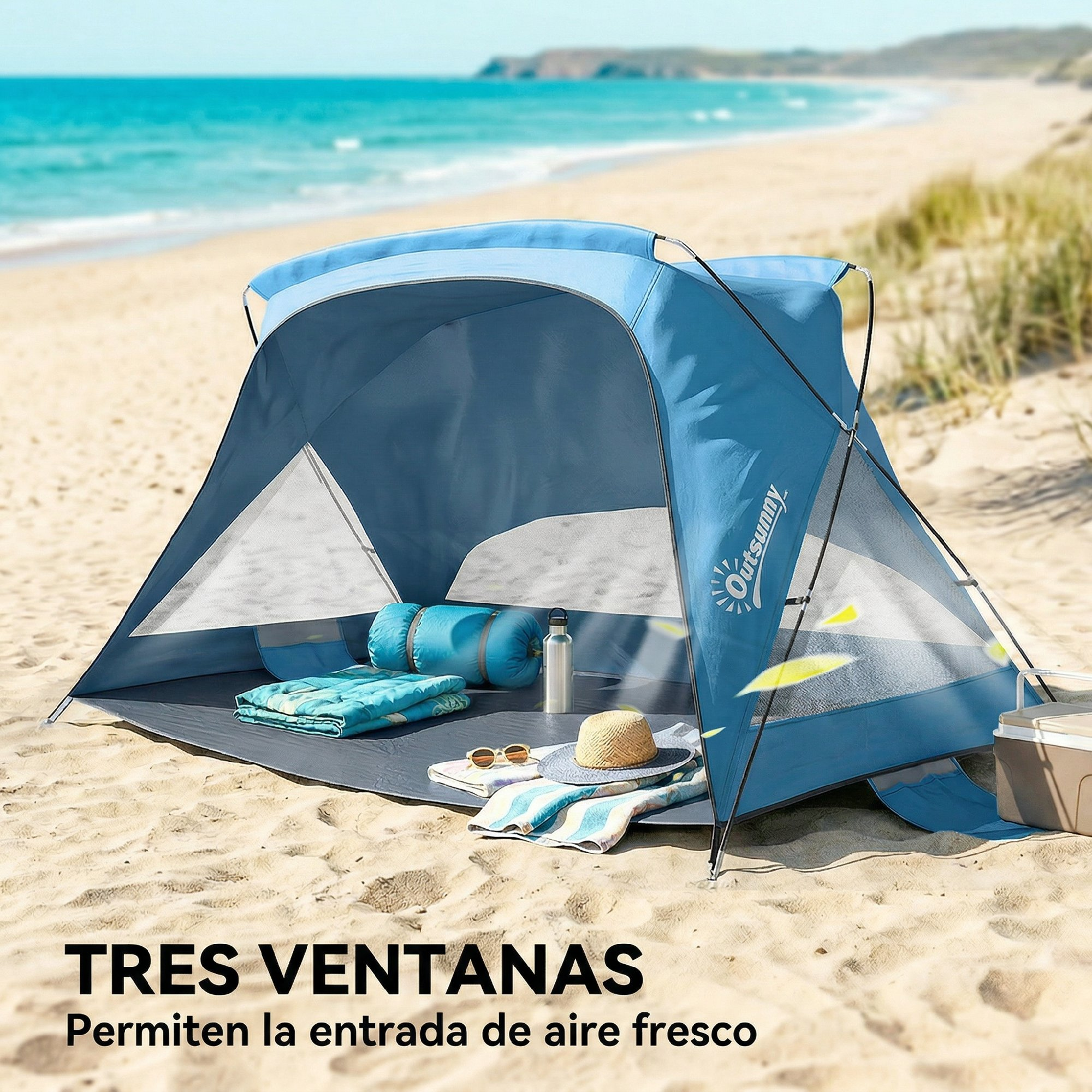 Una carpa de playa azul con mantas, almohadas y sombrero en la arena junto al mar.