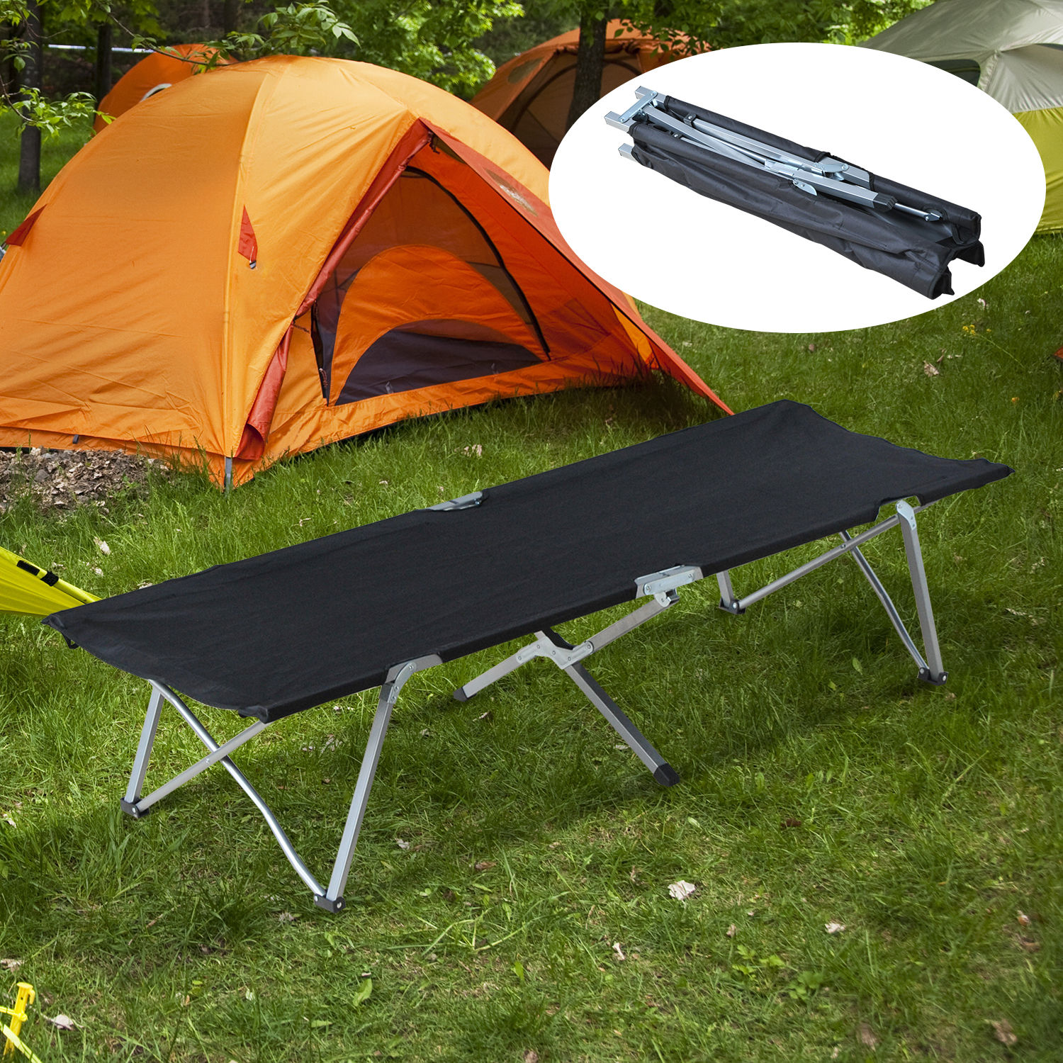 Una cama de camping negra de tela con marco metálico está montada sobre hierba verde, con tiendas al fondo.