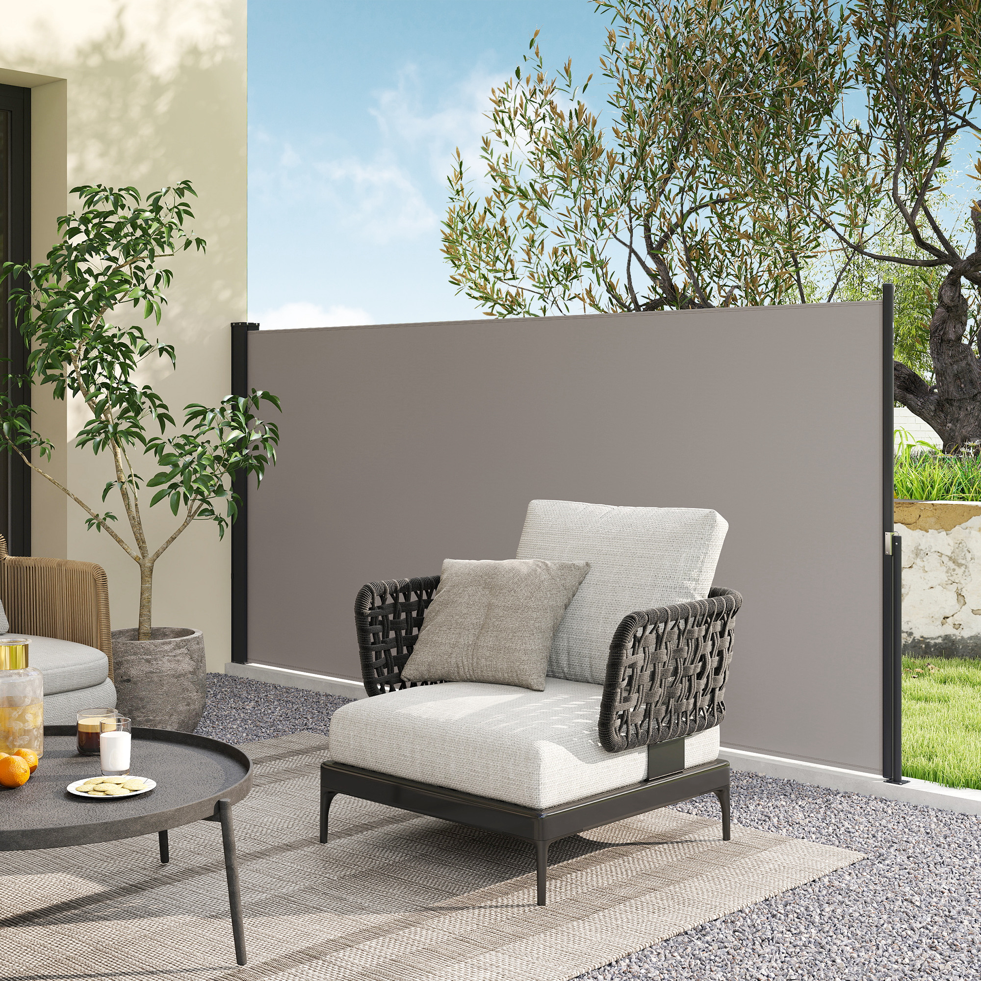 Un sillón moderno con cojines se sienta en un patio de grava junto a una mesa con naranjas.