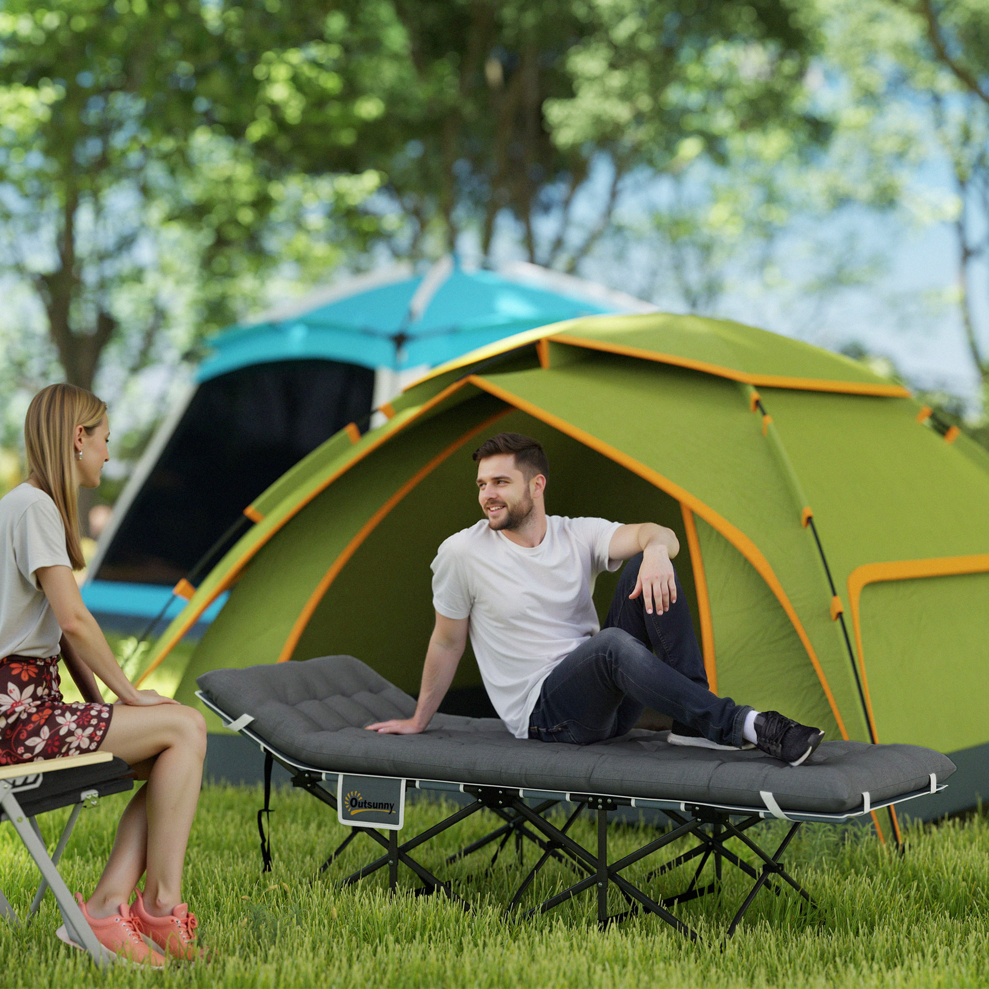 Un hombre y una mujer se relajan al aire libre cerca de tiendas de campaña en un camping.