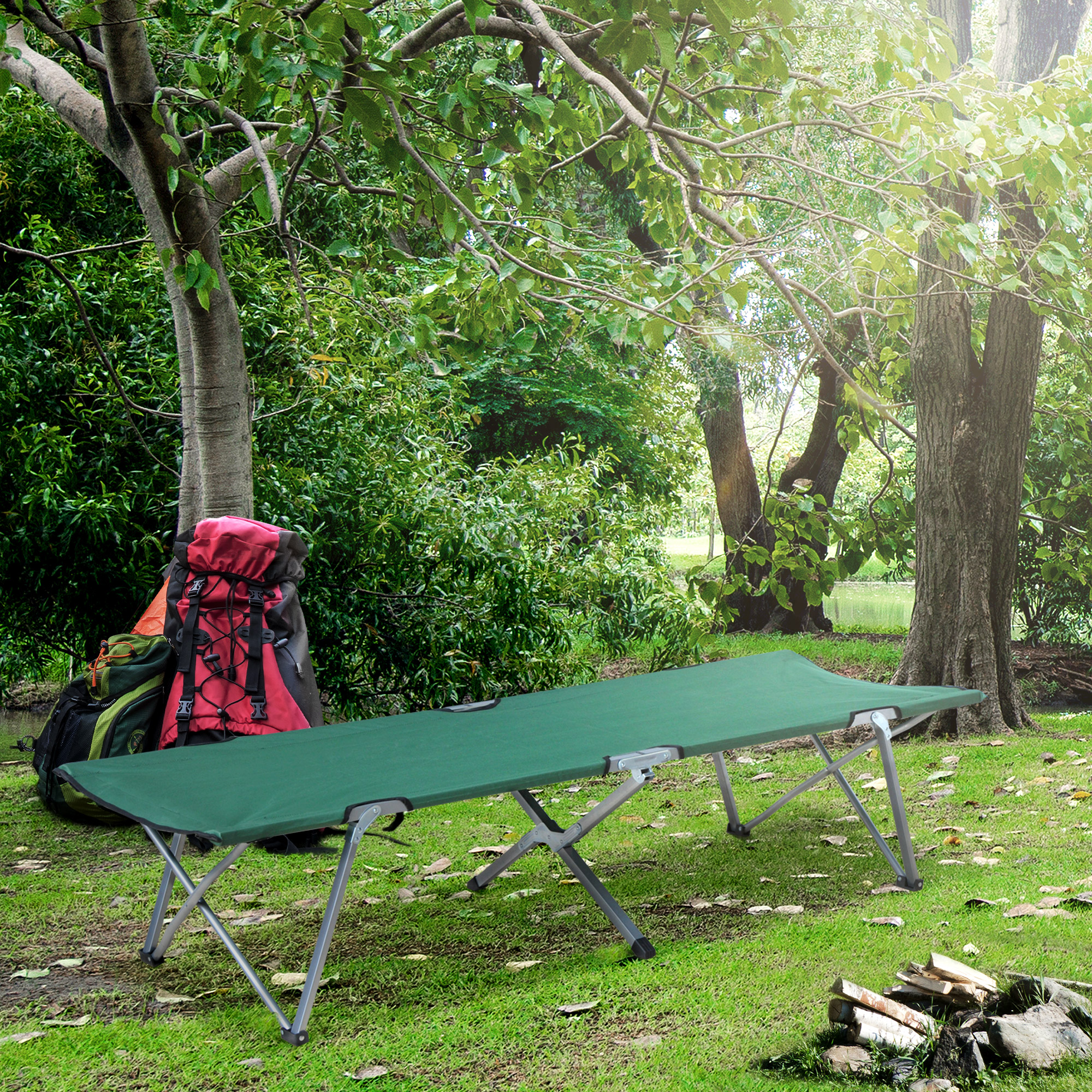 Una catre de camping verde descansa sobre césped, con mochilas y árboles al fondo.
