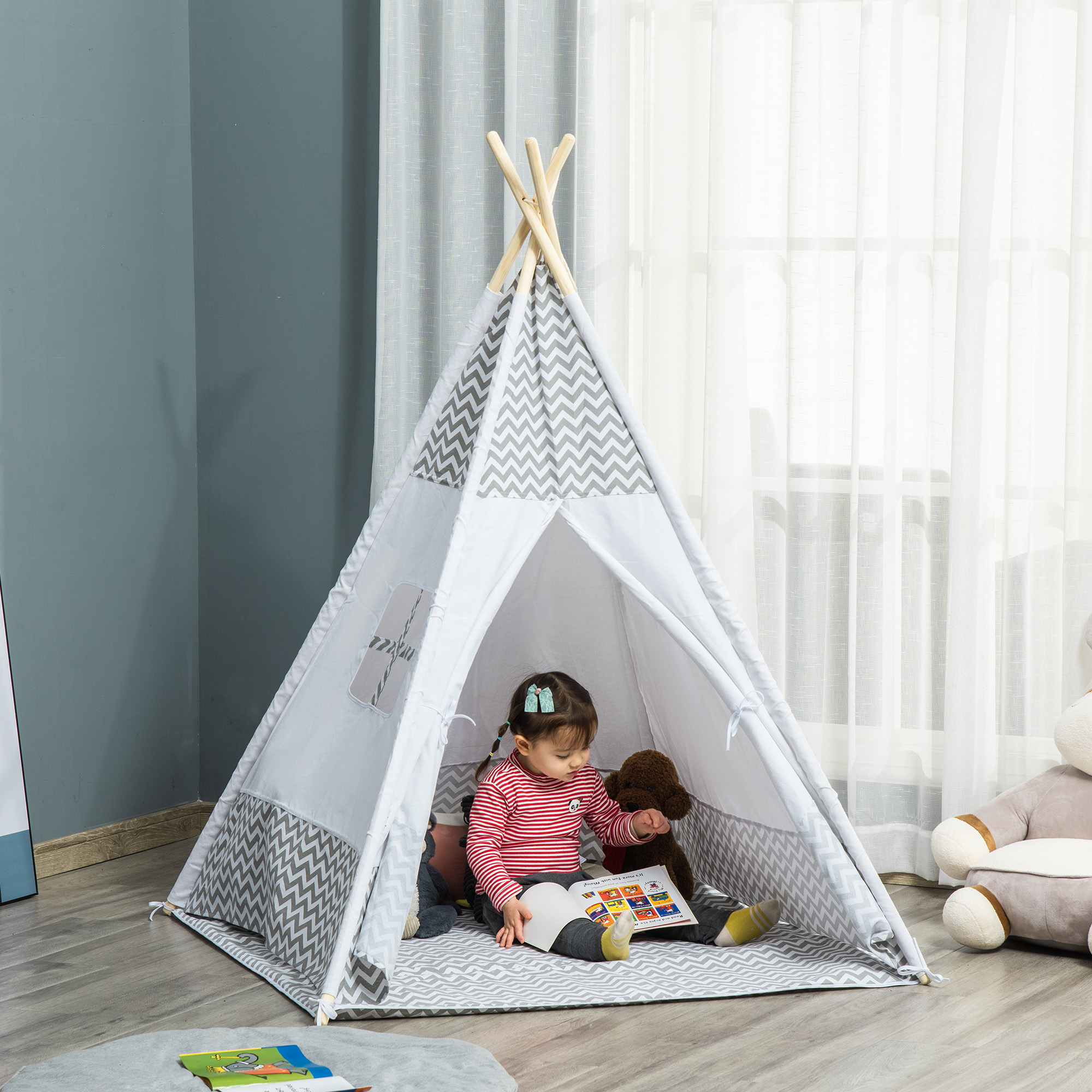 Una niña pequeña lee un libro dentro de una tienda tipi con peluches.