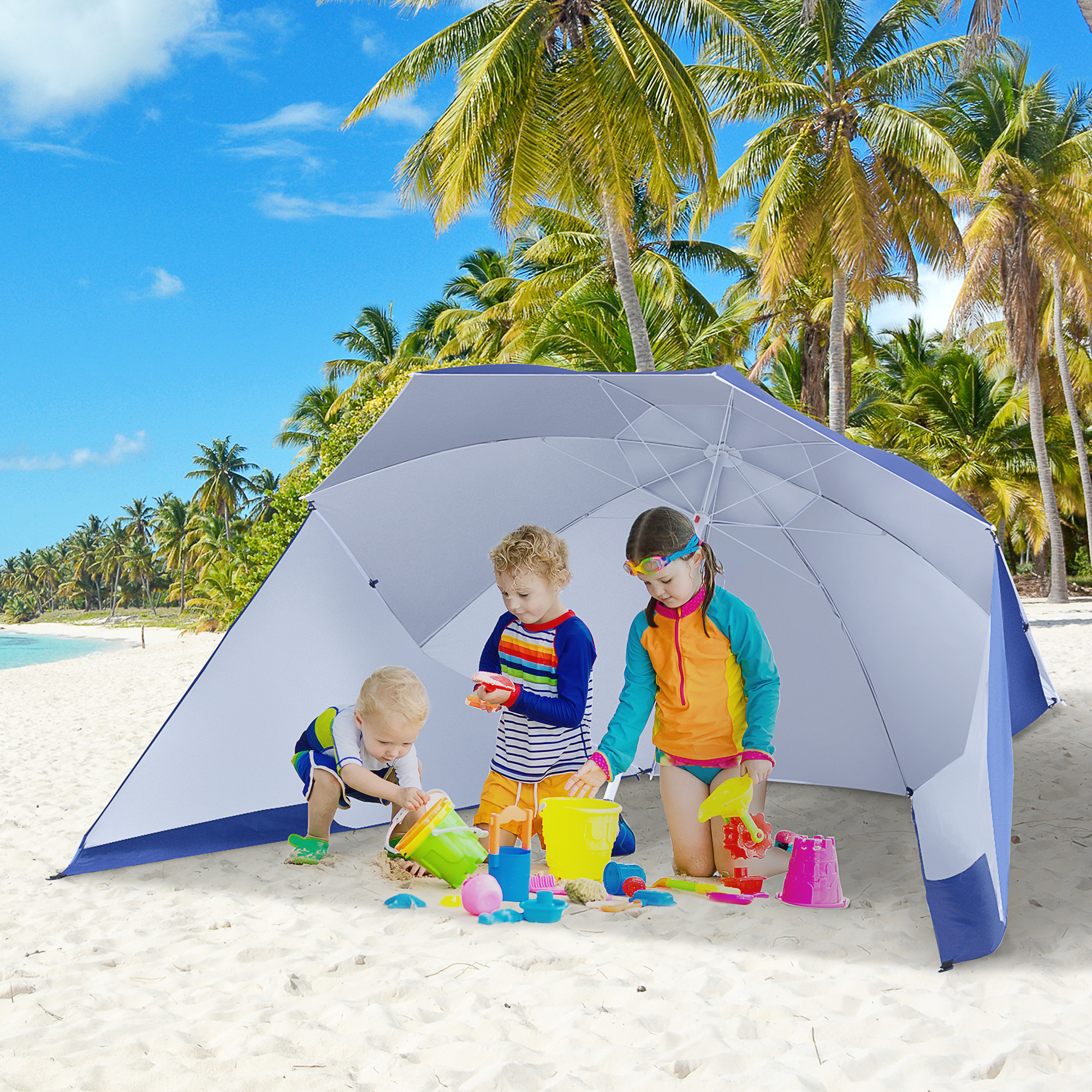 Tres niños juegan con juguetes de arena bajo una carpa de playa con palmeras al fondo.