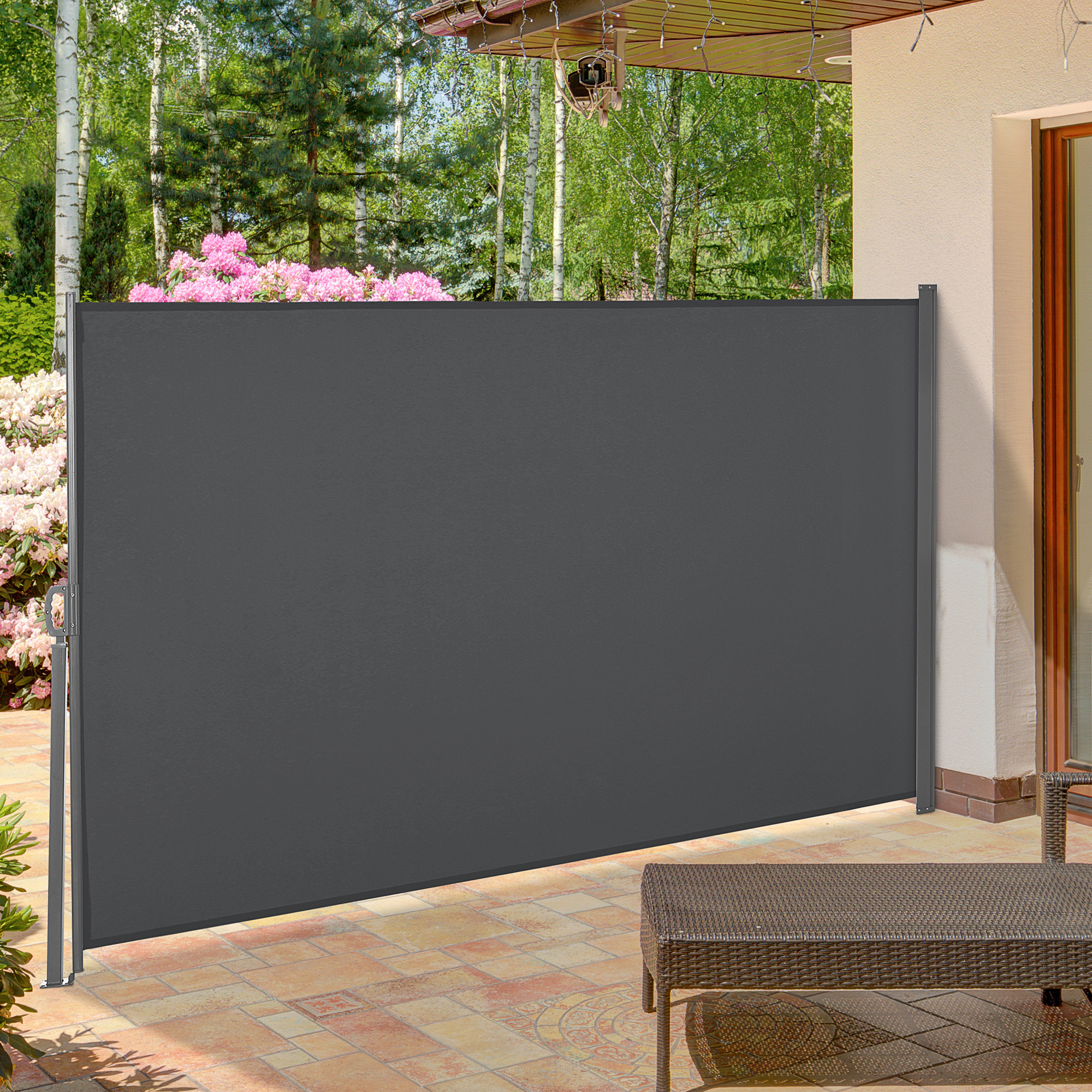 Una pantalla retráctil gris en un patio con flores y árboles al fondo.