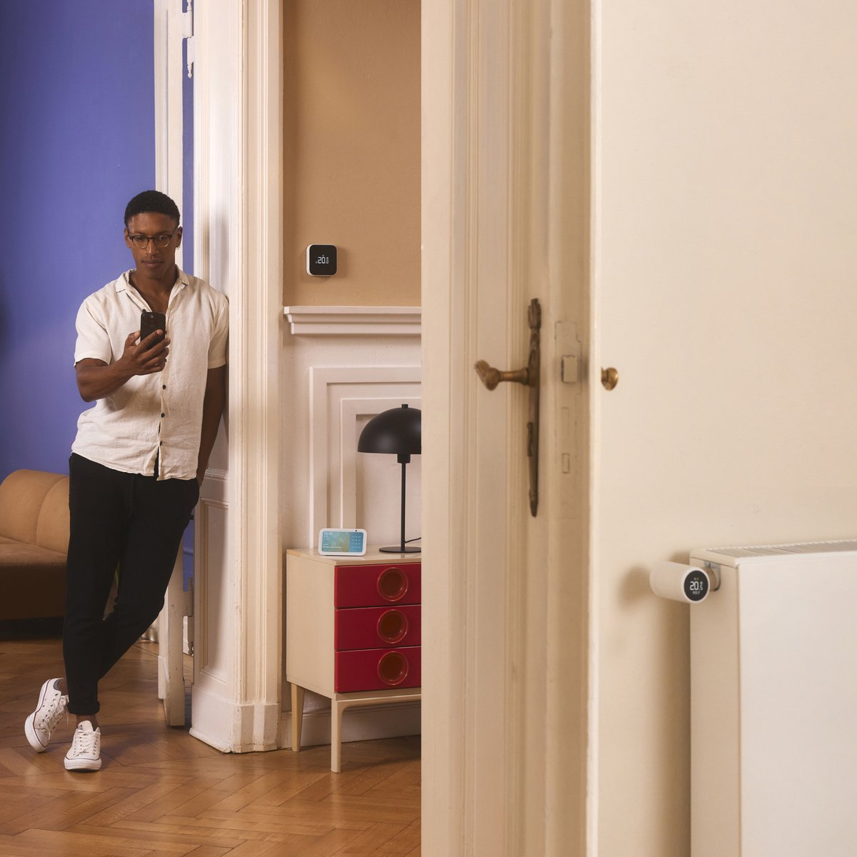 Man with smartphone leans on doorframe. Radiator thermostat on heating.