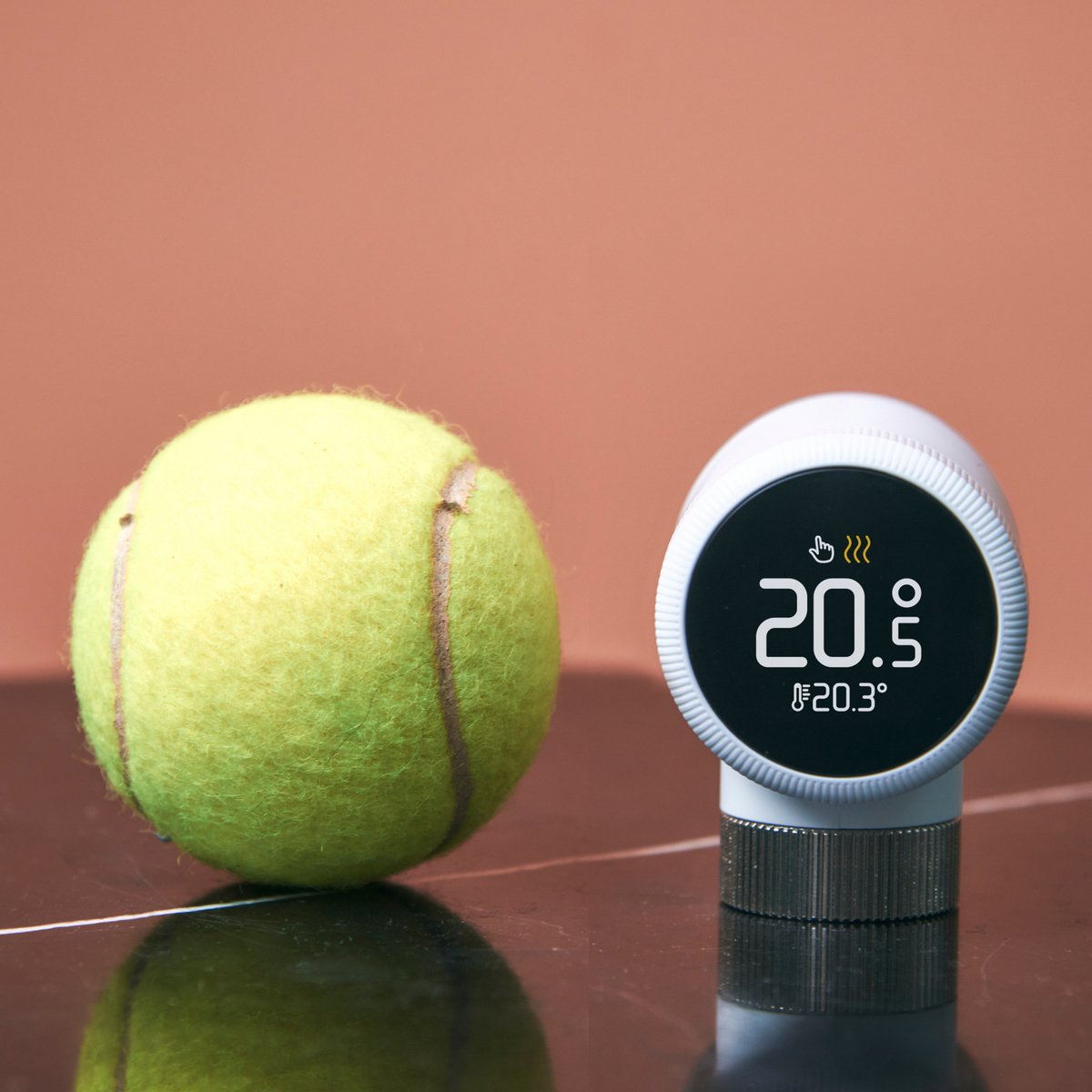 A yellow tennis ball sits beside a white digital thermostat on a dark surface.