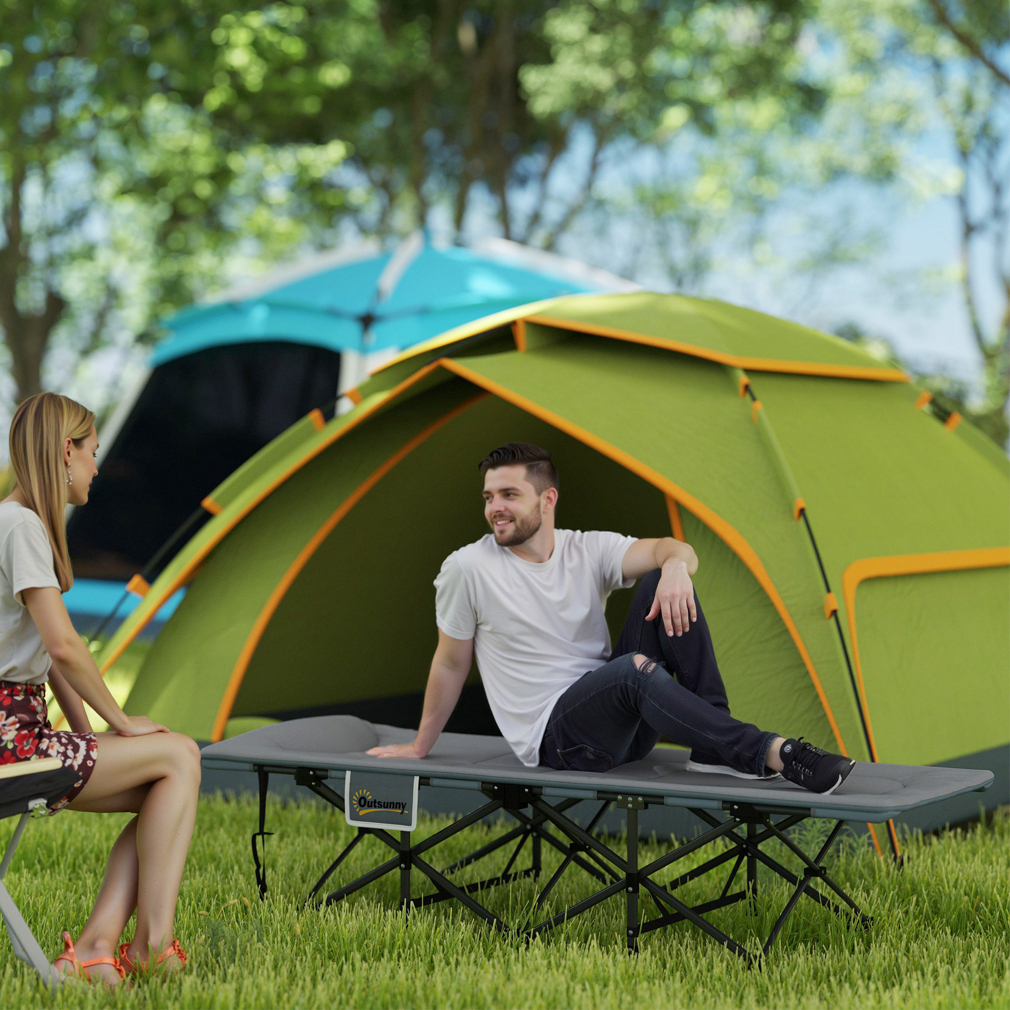 Una pareja se sienta en una cama de camping frente a tiendas de campaña al aire libre.