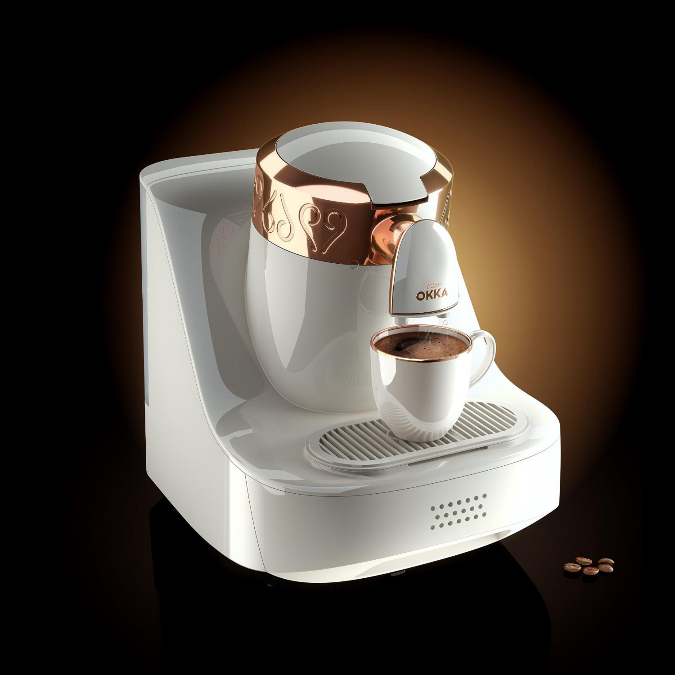 Eine weiße Kaffeemaschine mit kupferfarbenen Akzenten und einer Tasse Kaffee.