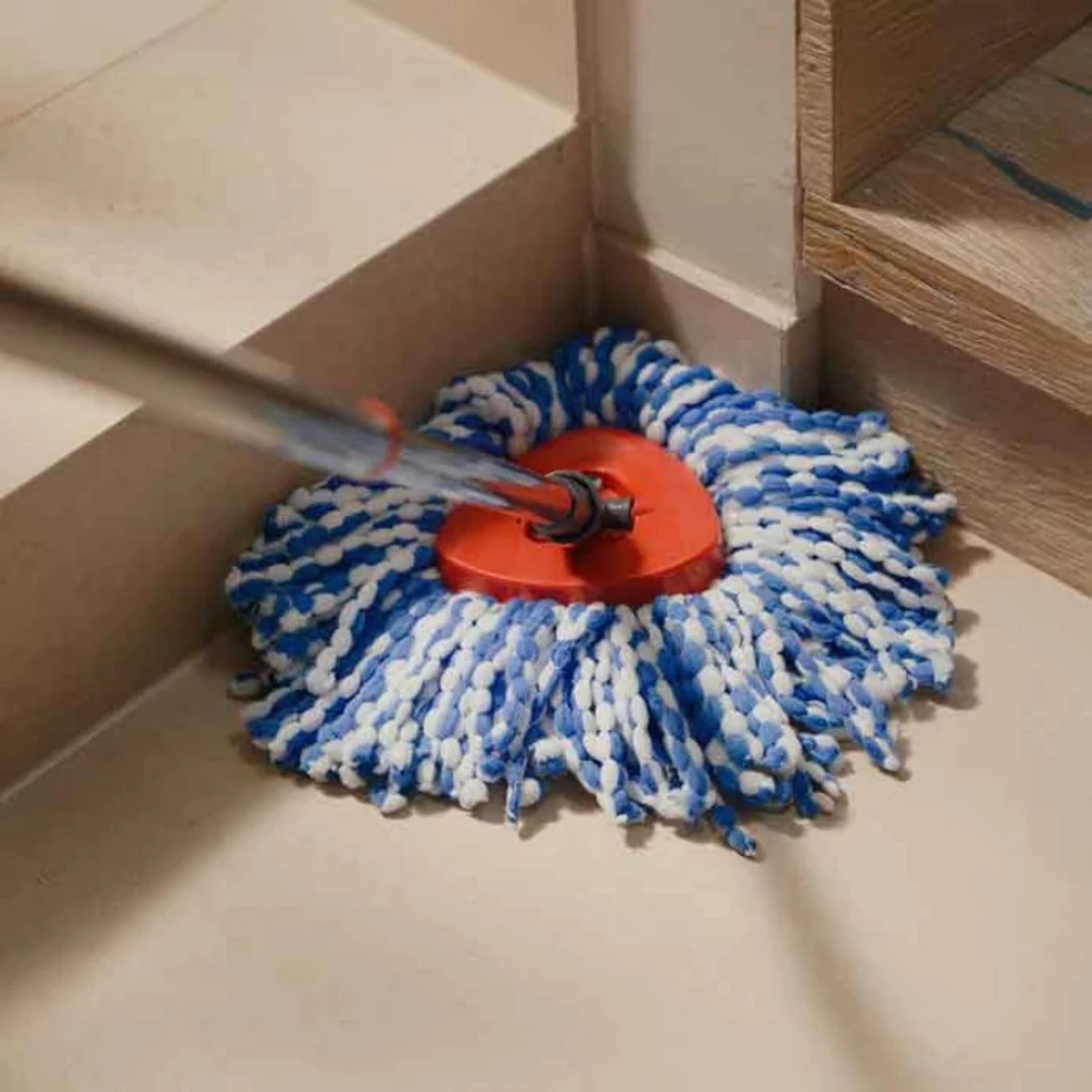 Un mocio blu e bianco con manico rosso poggia su un pavimento piastrellato.