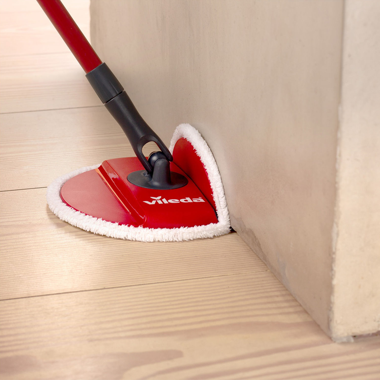 Mocio rosso Vileda con bordo bianco pulisce angolo su pavimento in legno.