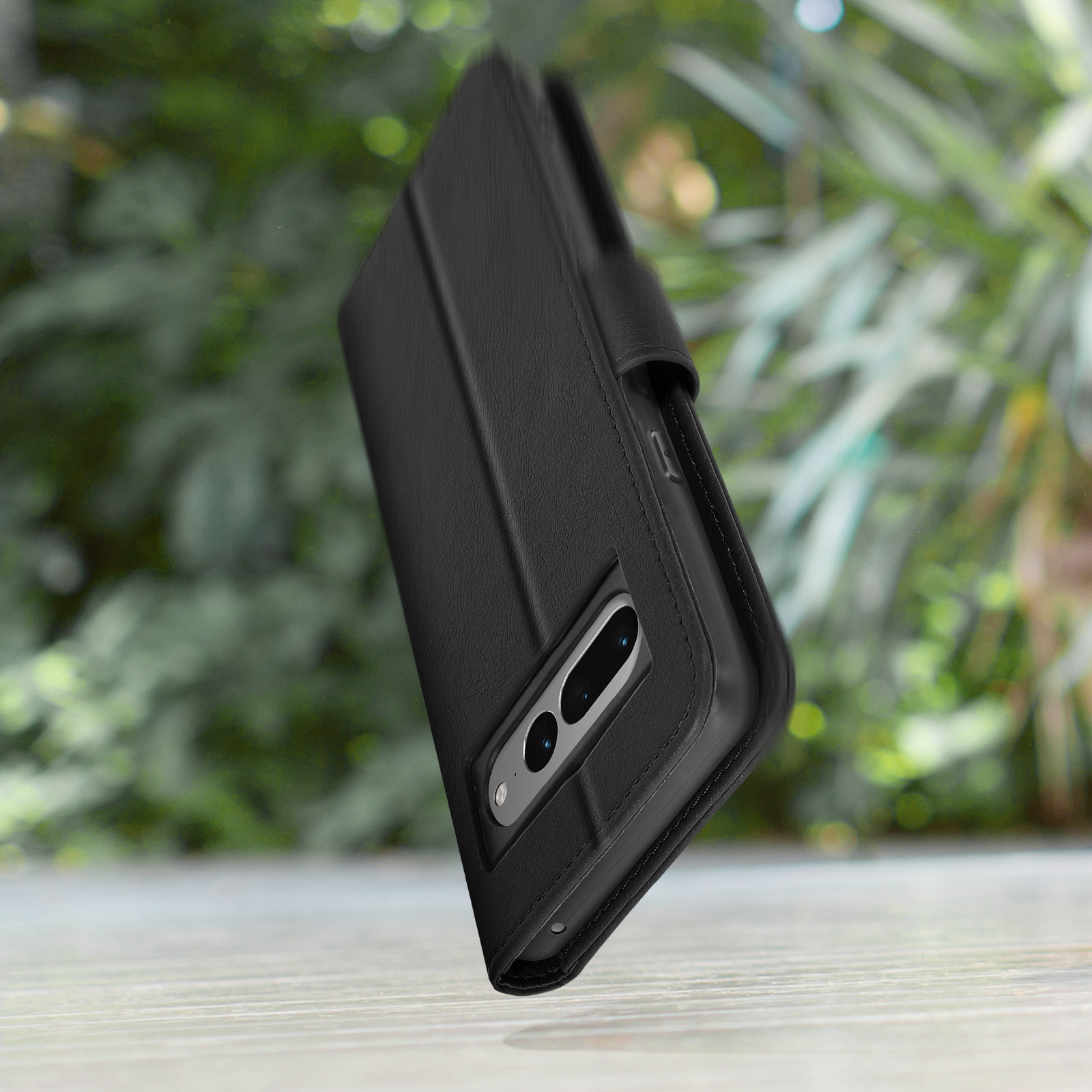 Custodia a libro in pelle nera per smartphone, fotocamera visibile su tavolo in legno.