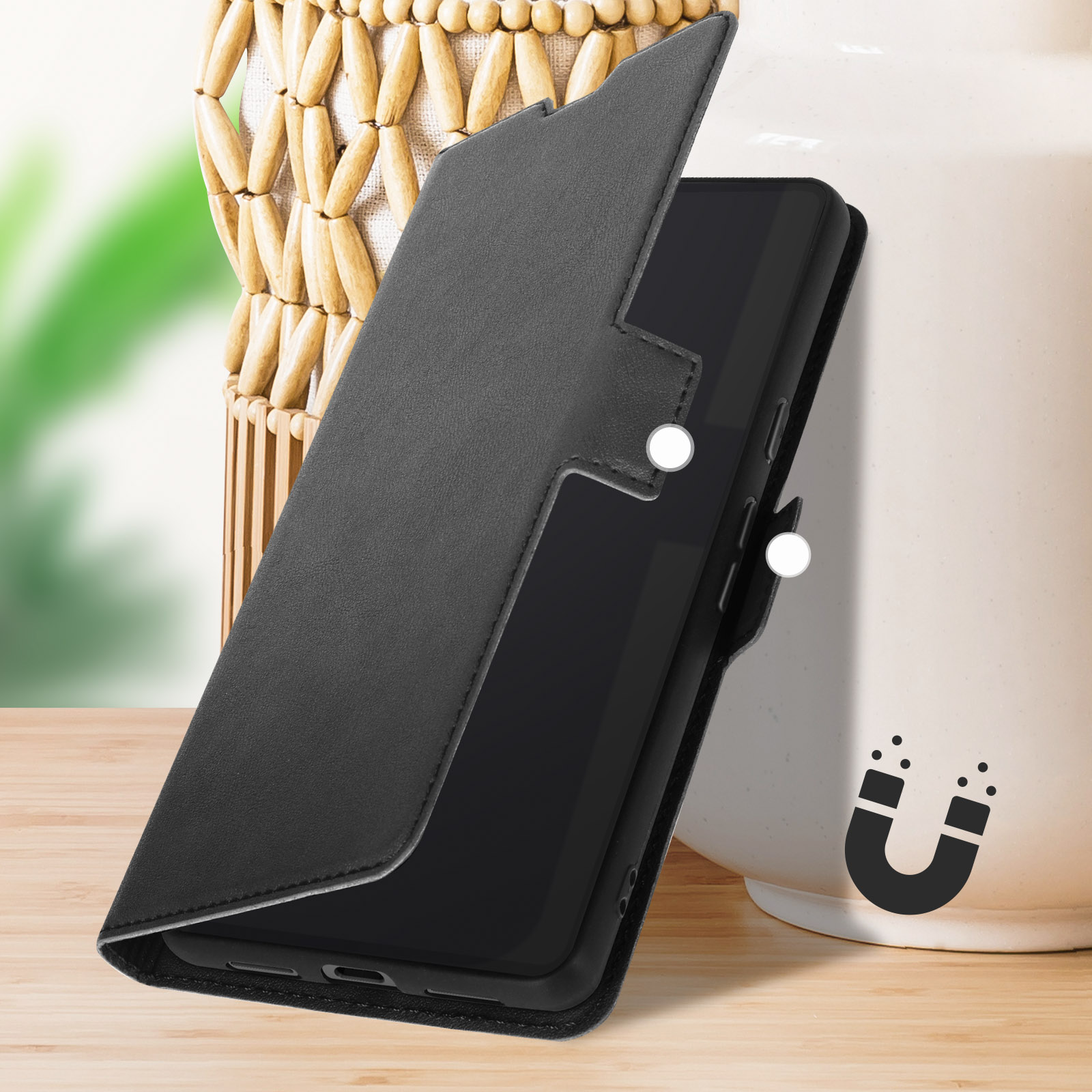 Una custodia per telefono in pelle nera è aperta, rivelando uno smartphone nero. Un cesto intrecciato è dietro.