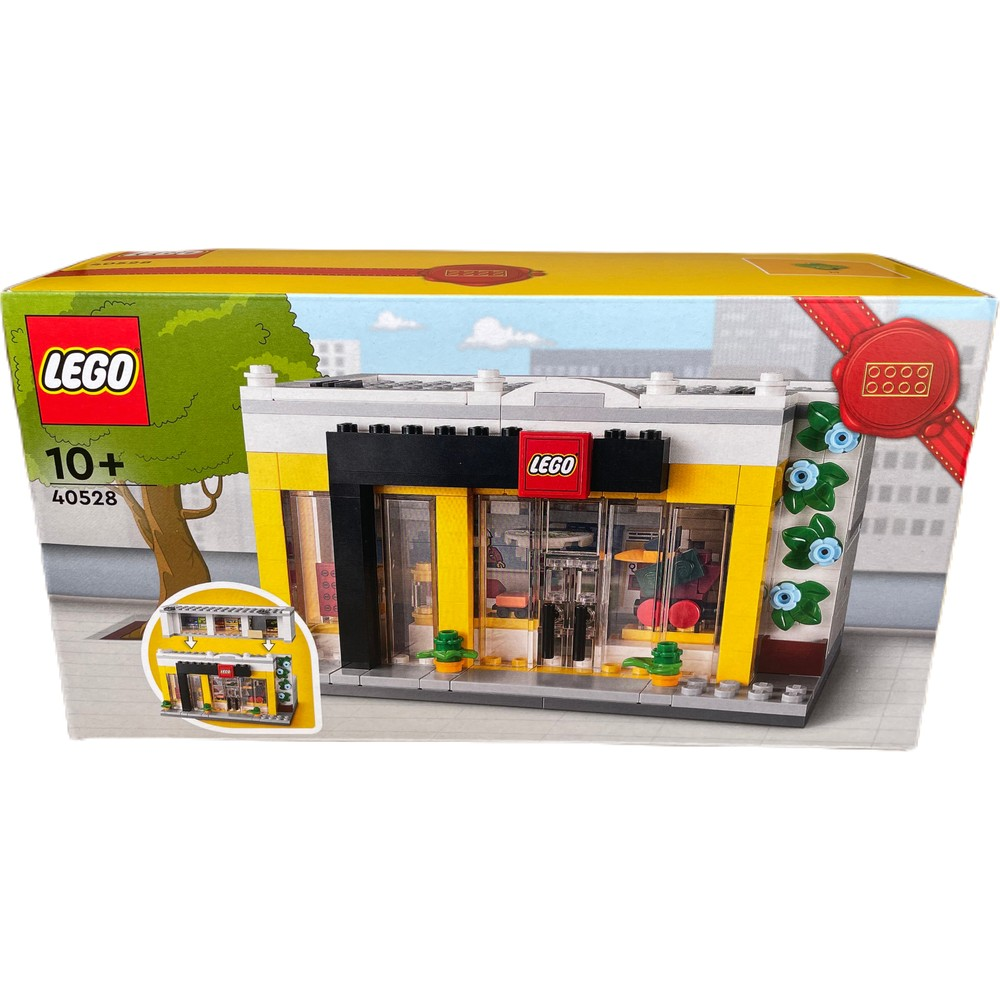 Sarı ve beyaz bina, yeşil ağaç ve gökyüzü olan Lego mağaza kutusu.