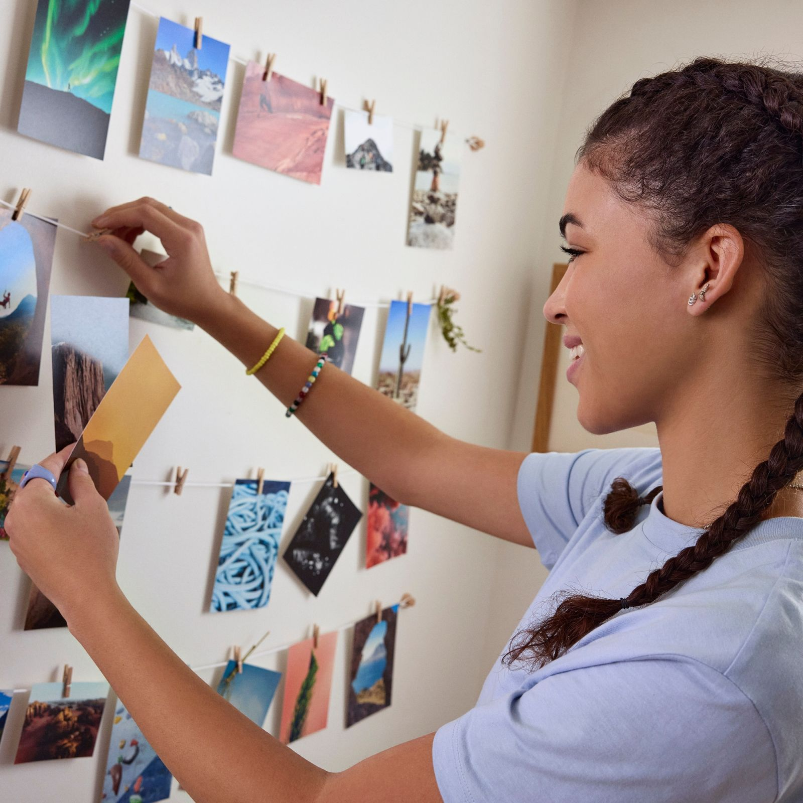 Een jonge vrouw hangt foto's met wasknijpers aan een touw tegen een witte muur.