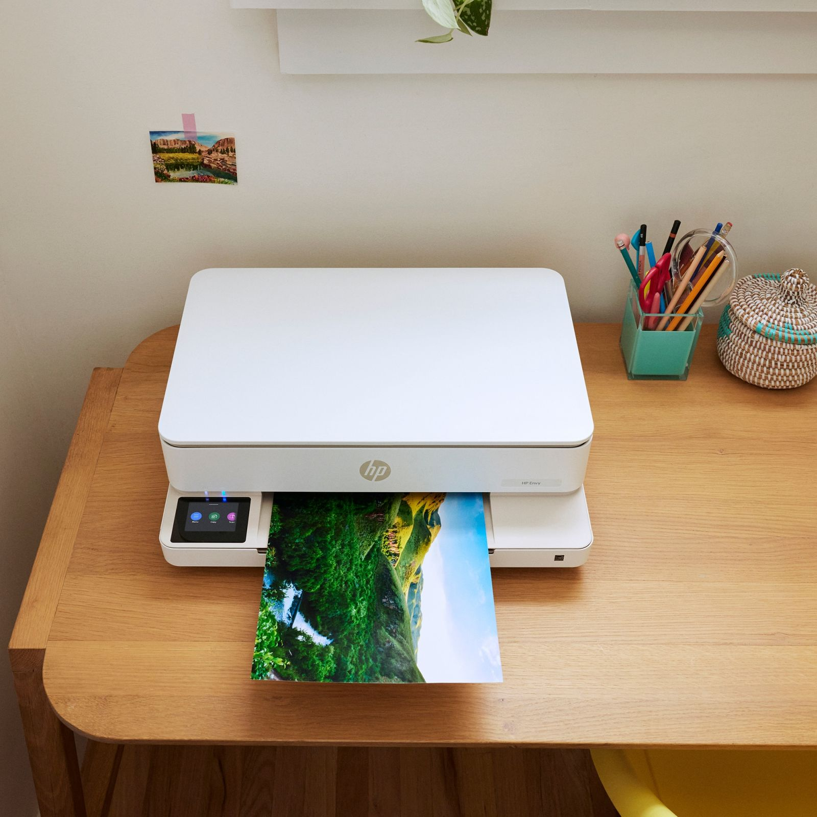 Een witte printer drukt een foto af van een groen landschap met blauwe lucht.